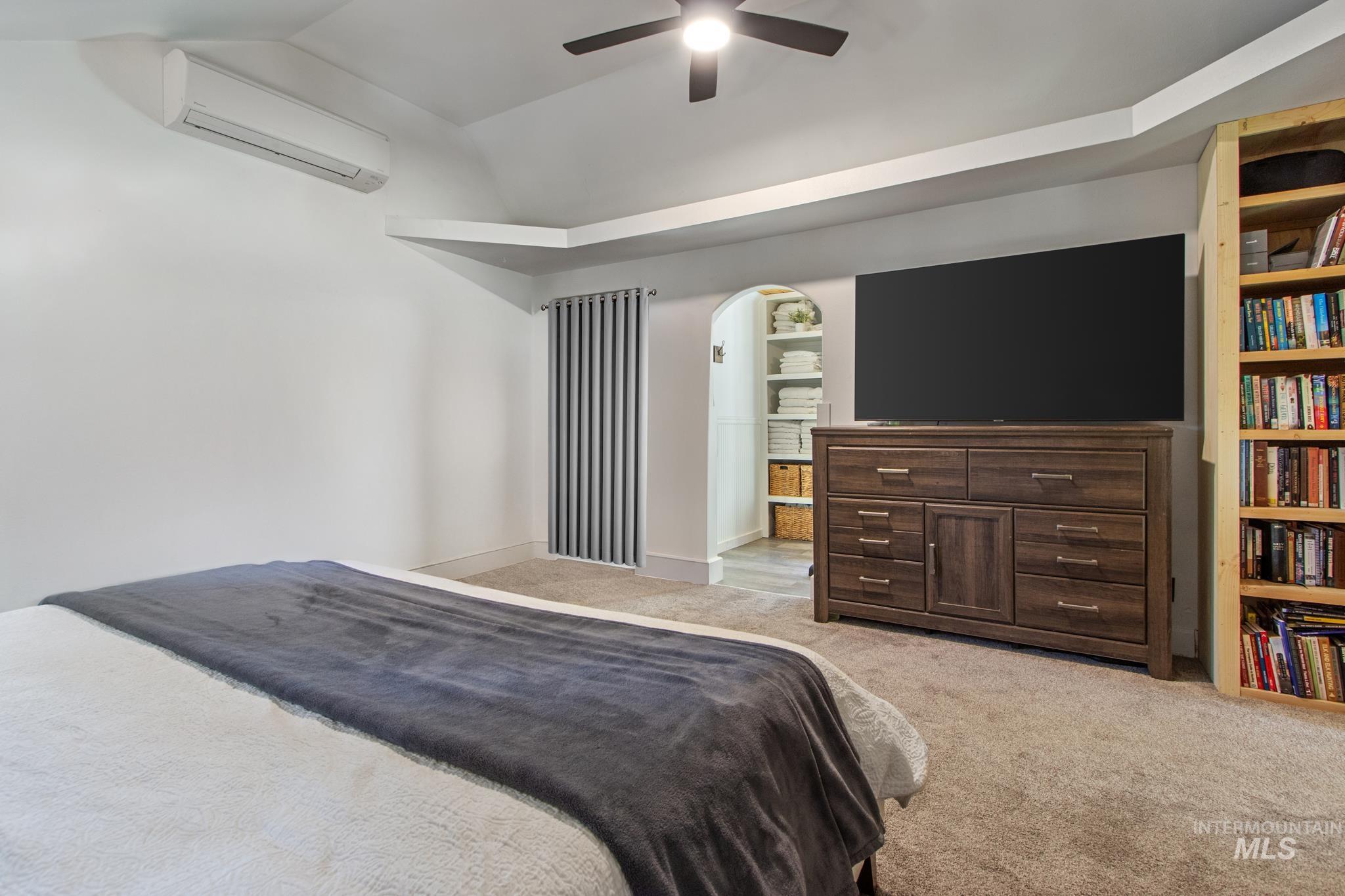 Bedroom with light carpet, a wall mounted AC, ceiling fan, vaulted ceiling, and arched walkways