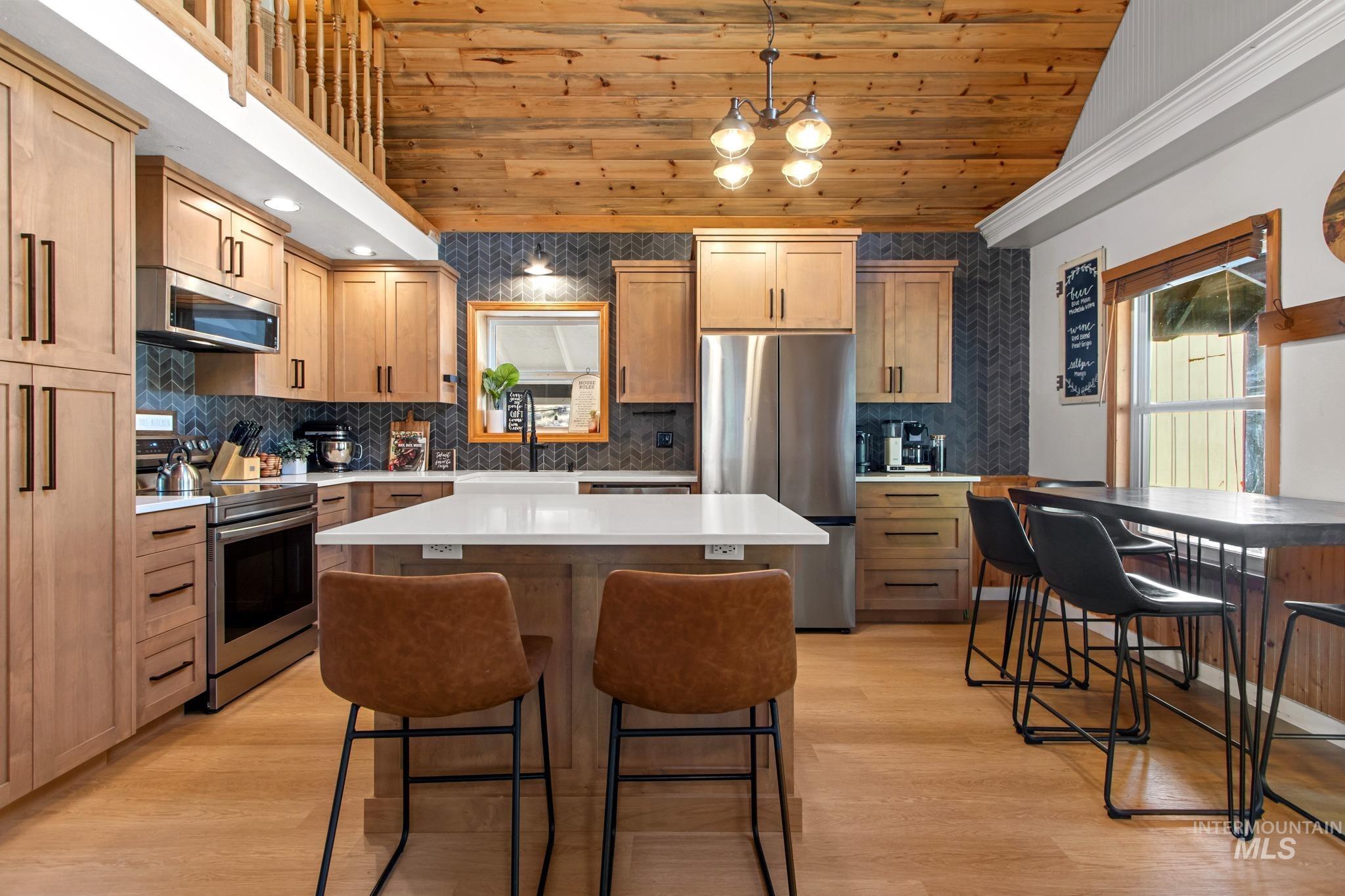 Kitchen with a kitchen island, appliances with stainless steel finishes, wood ceiling, a breakfast bar, and light wood-style flooring