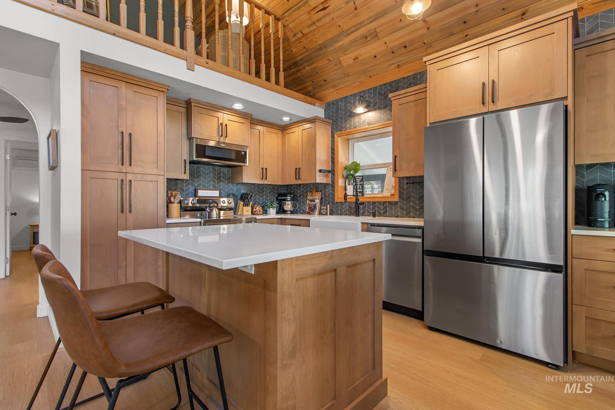Kitchen featuring stainless steel appliances, tasteful backsplash, a kitchen island, a kitchen bar, and wooden ceiling
