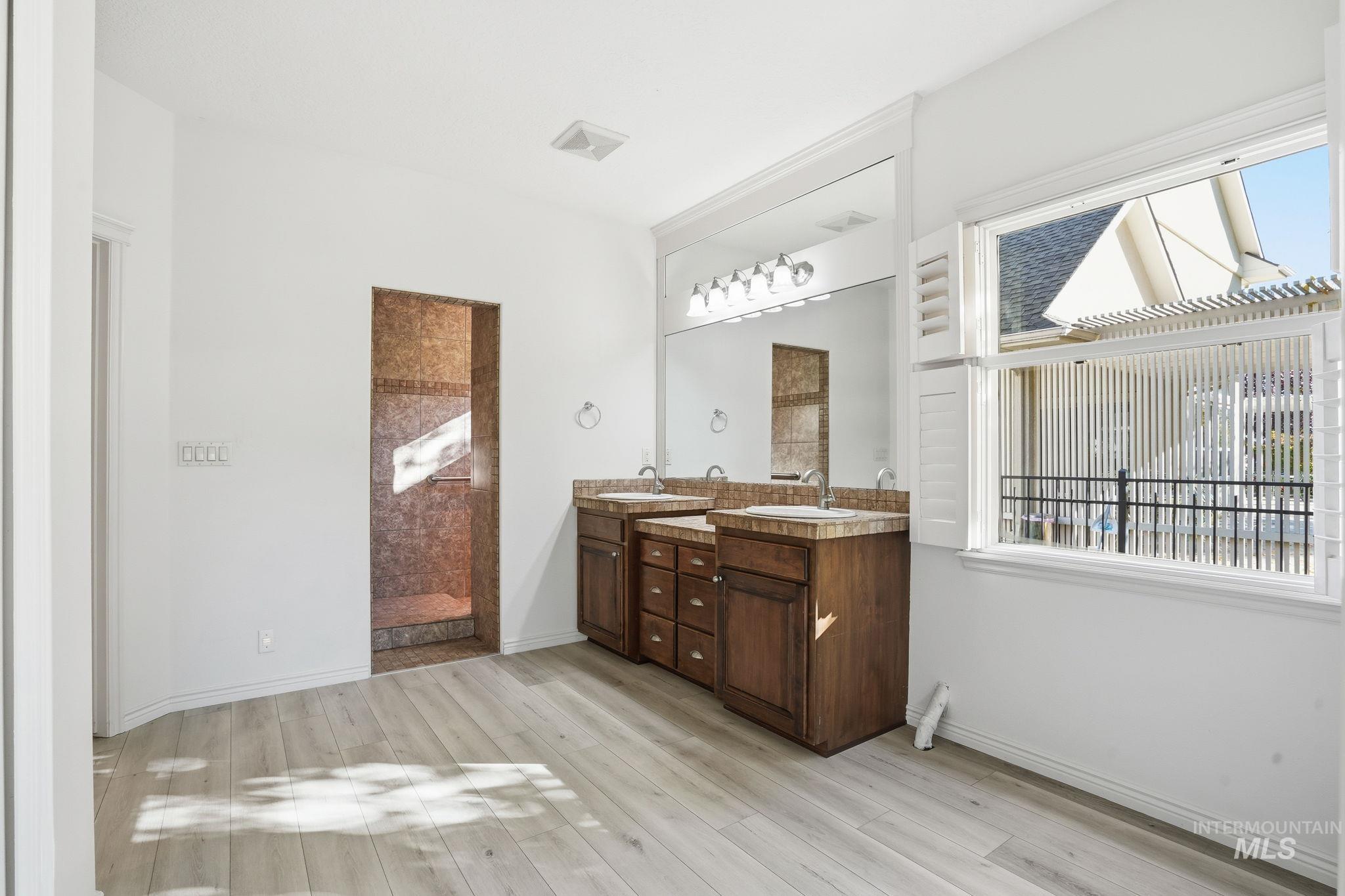 Bathroom with double vanity, light wood-style flooring, and a walk in shower