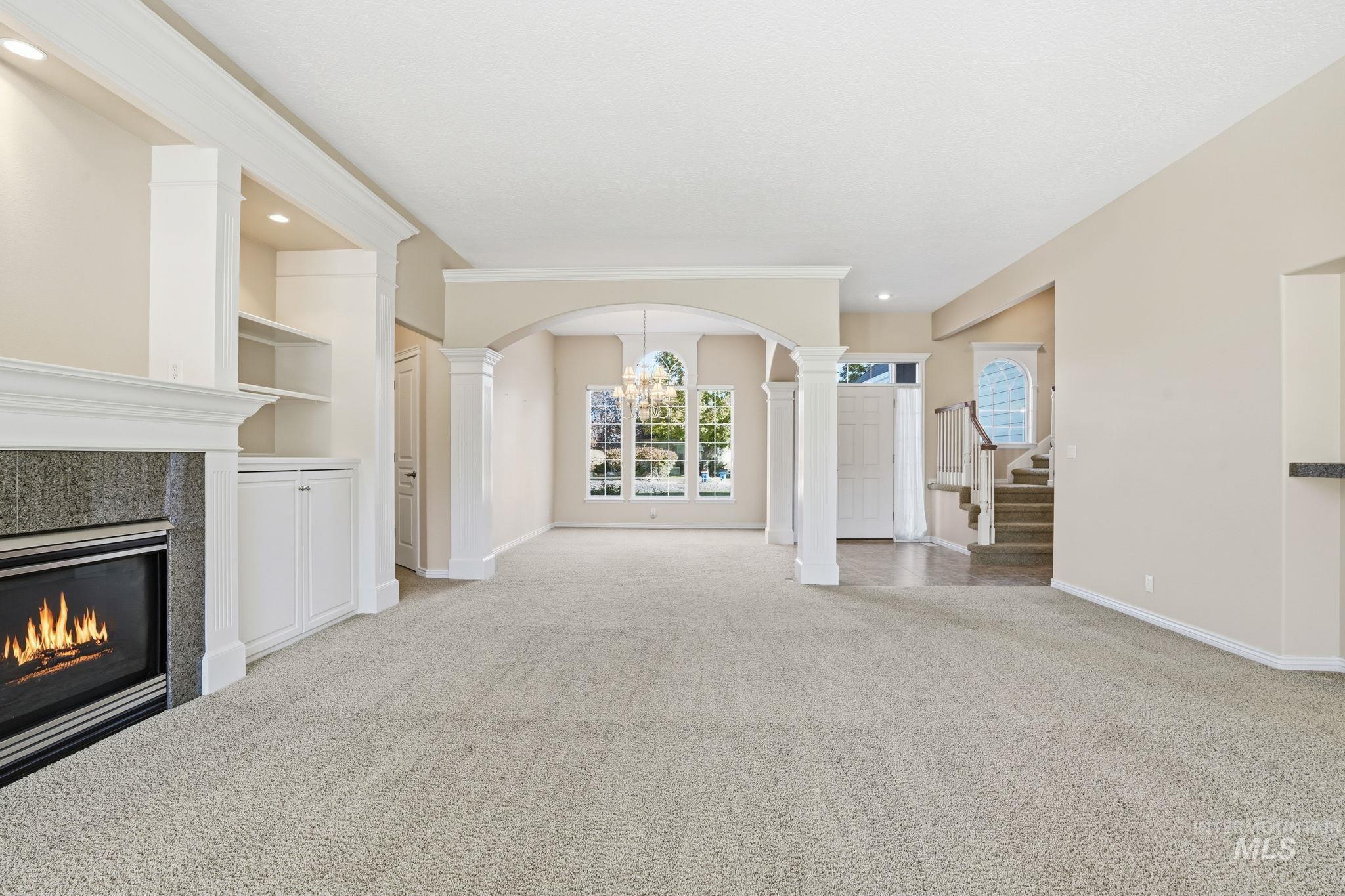 Unfurnished living room with a chandelier, light colored carpet, a tile fireplace, stairway, and decorative columns