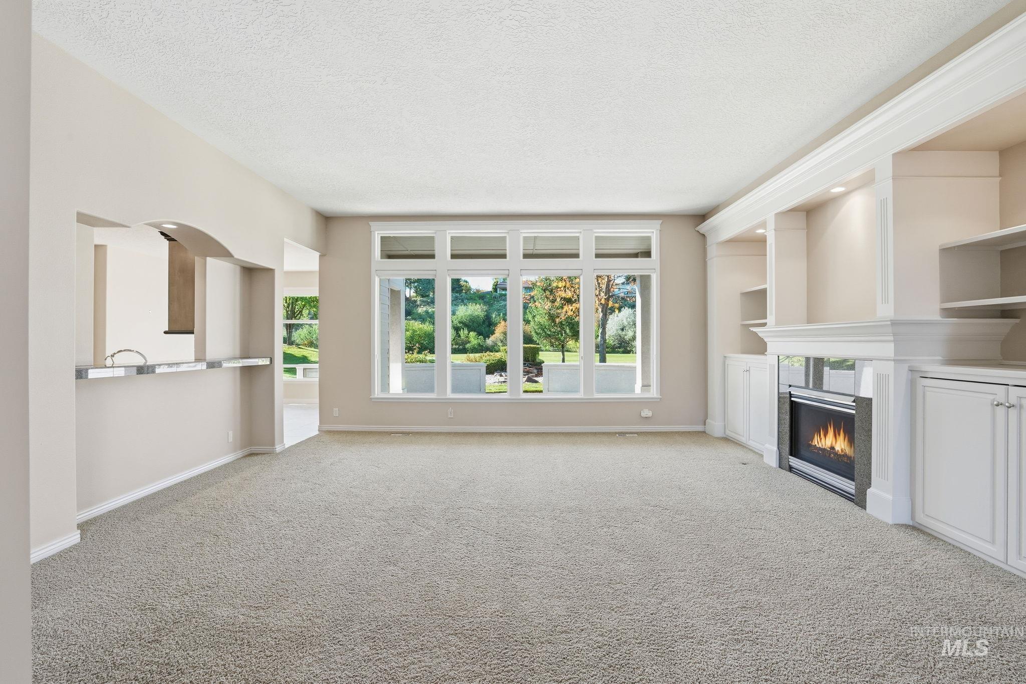 Unfurnished living room featuring light carpet, a textured ceiling, and a glass covered fireplace