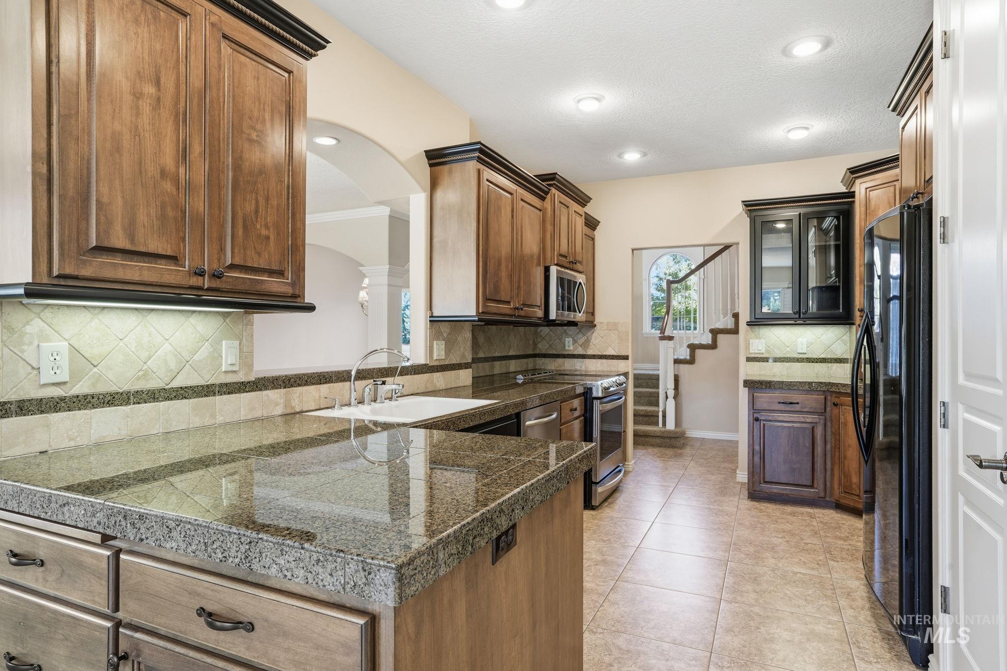 Kitchen with tile counters, stainless steel appliances, light tile patterned floors, decorative backsplash, and recessed lighting