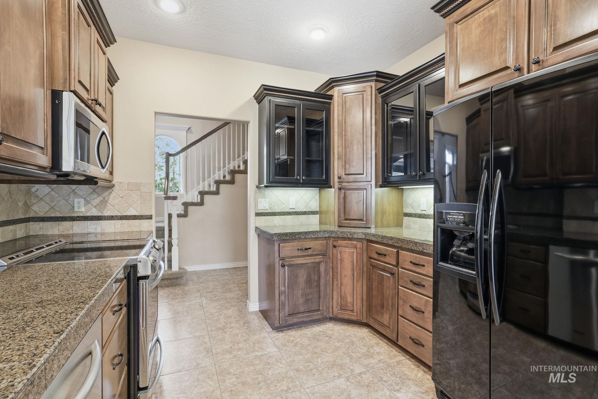 Kitchen featuring stainless steel appliances, a textured ceiling, backsplash, light tile patterned floors, and glass insert cabinets