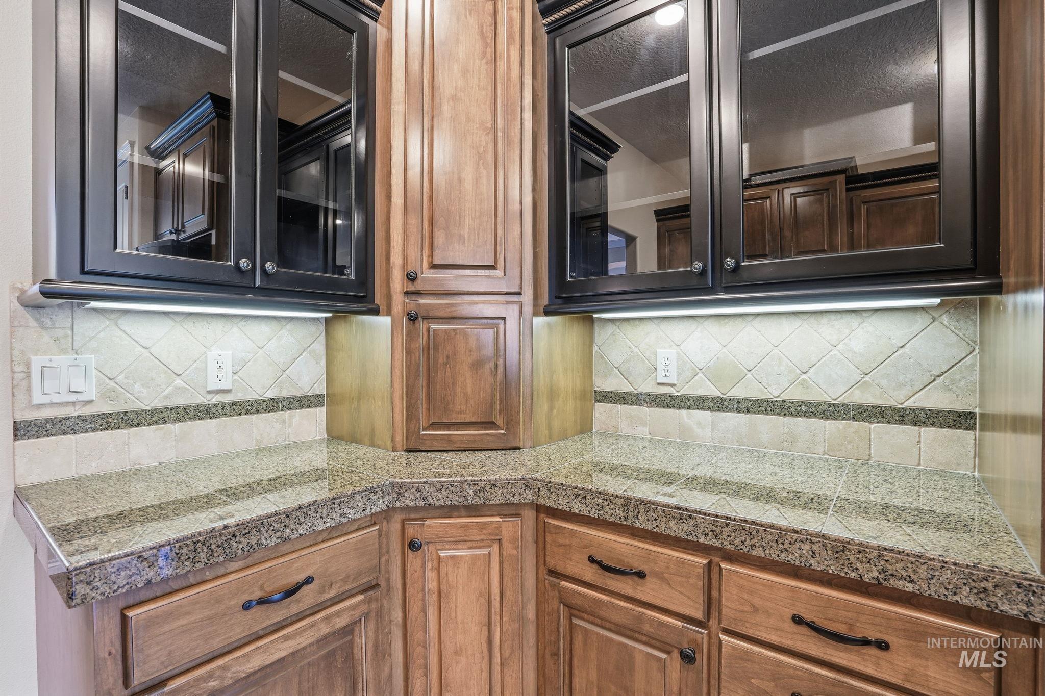 Kitchen with tile counters, glass insert cabinets, decorative backsplash, and brown cabinets