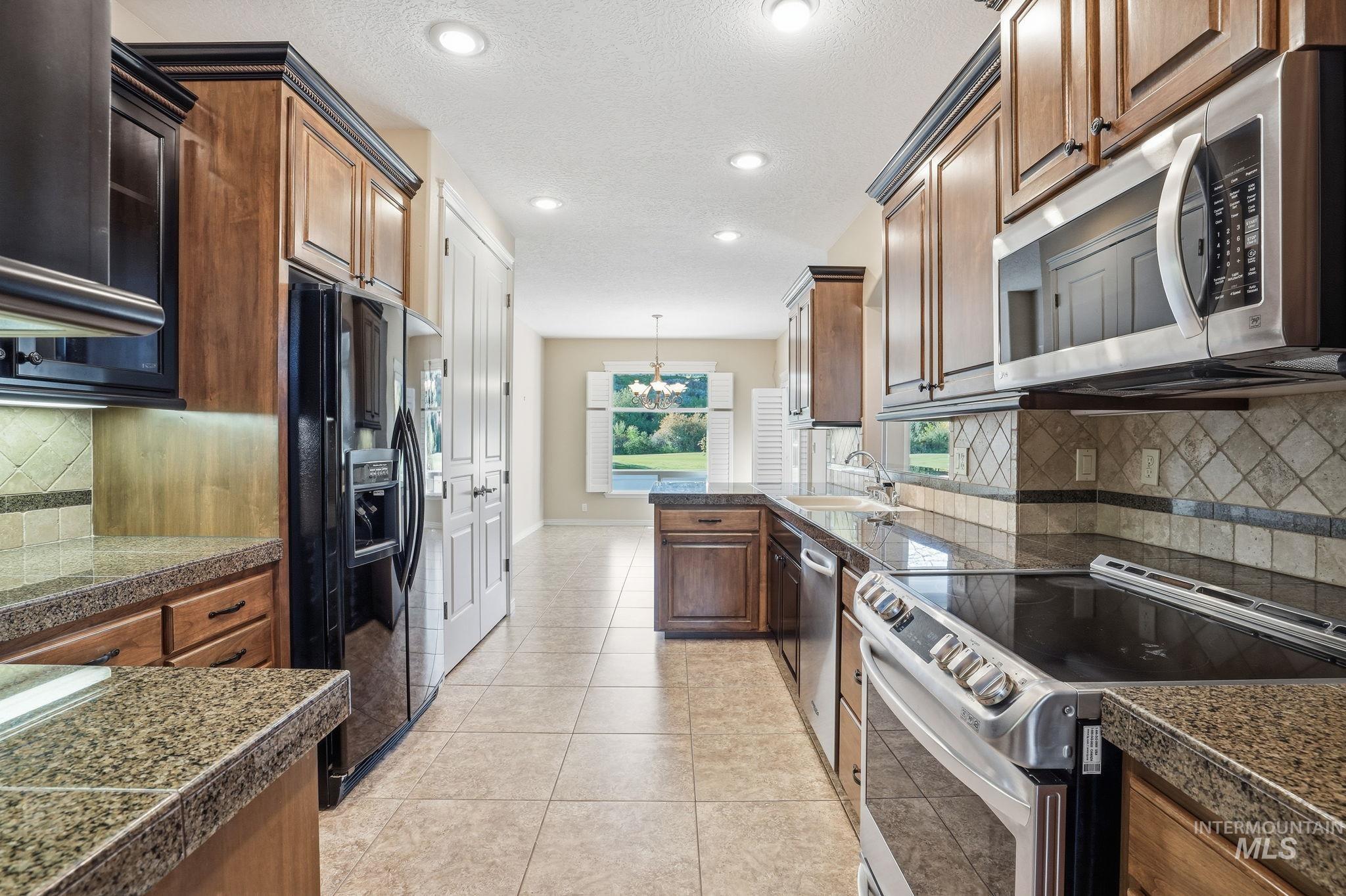 Kitchen with tile countertops, backsplash, stainless steel appliances, decorative light fixtures, and recessed lighting