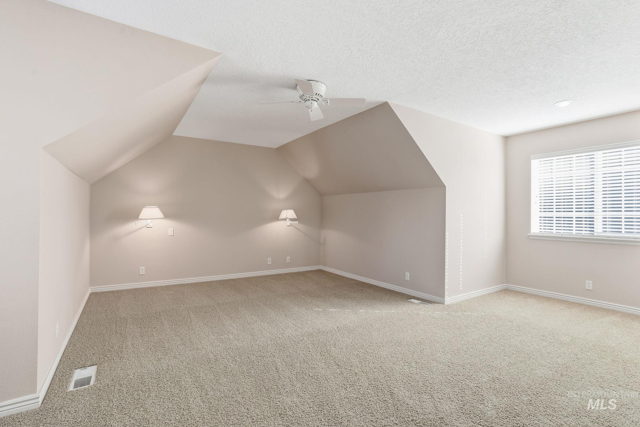 Bonus room with light carpet, lofted ceiling, a ceiling fan, and a textured ceiling