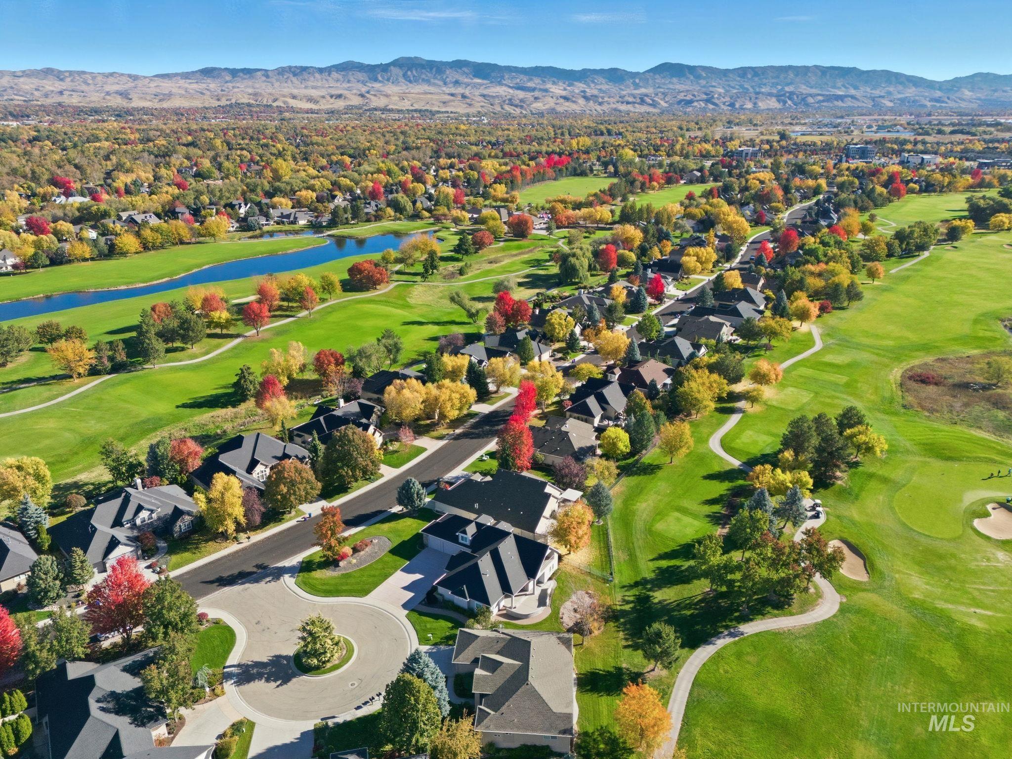 Aerial view of property and surrounding area featuring a golf club, nearby suburban area, and a water and mountain view