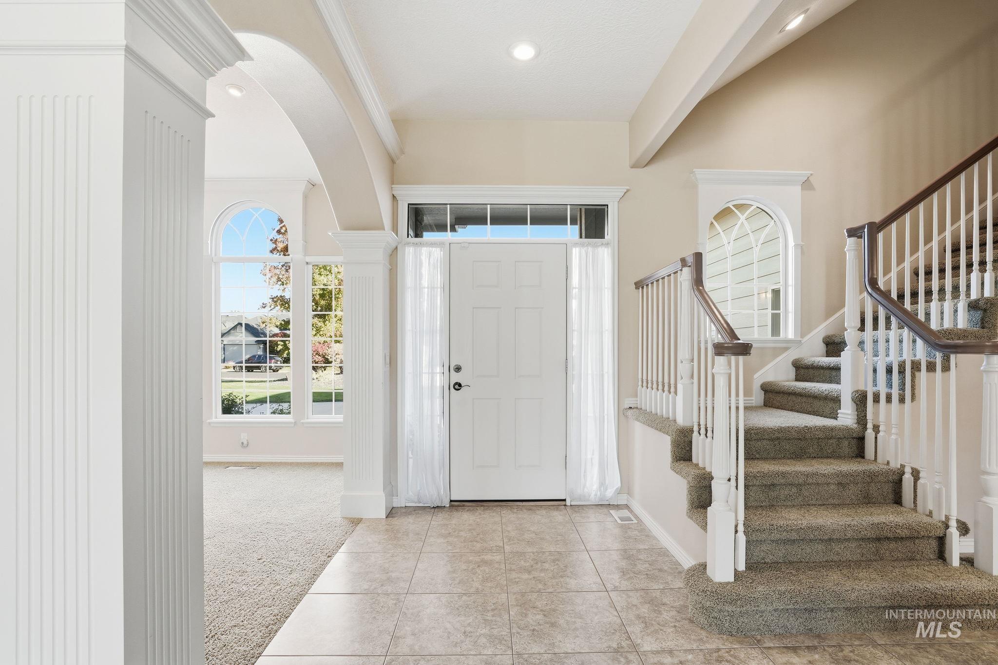Entrance foyer with light carpet, arched walkways, light tile patterned flooring, stairway, and beamed ceiling