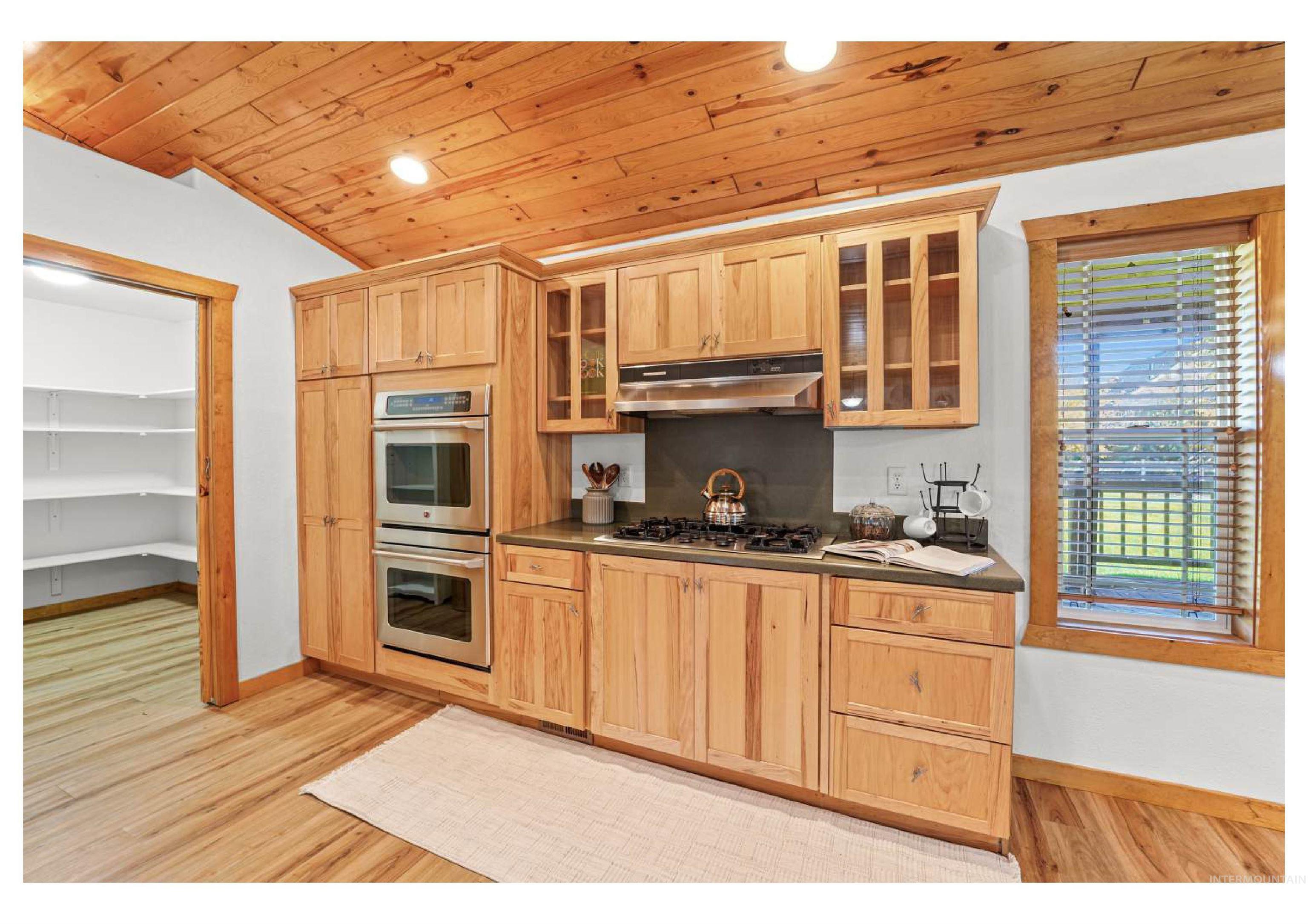 Kitchen featuring glass insert cabinets, dark countertops, light brown cabinetry, wooden ceiling, and stainless steel appliances