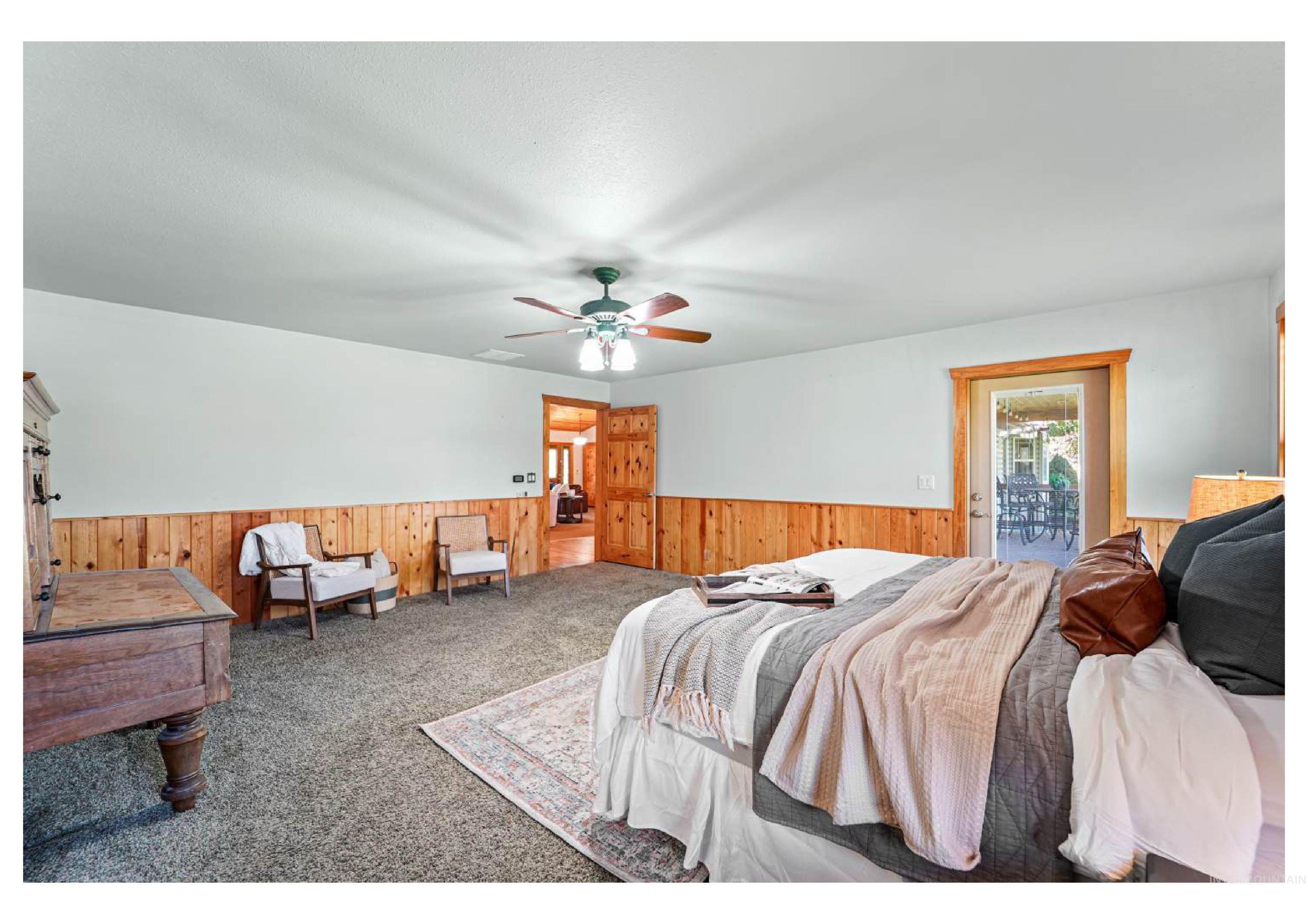 Carpeted bedroom with wooden walls, ceiling fan, access to outside, and a wainscoted wall