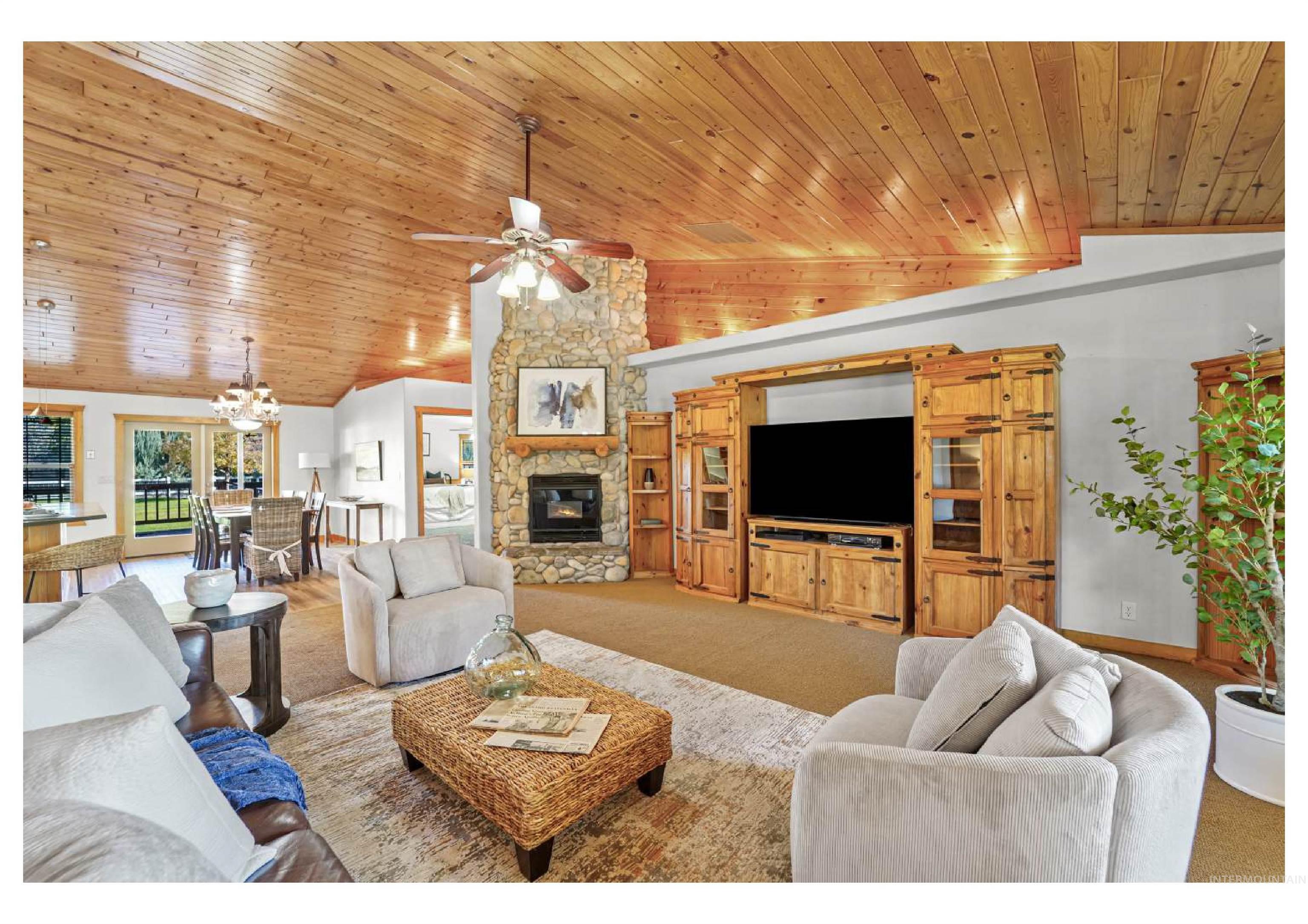 Living room featuring carpet floors, a stone fireplace, wood ceiling, a chandelier, and ceiling fan