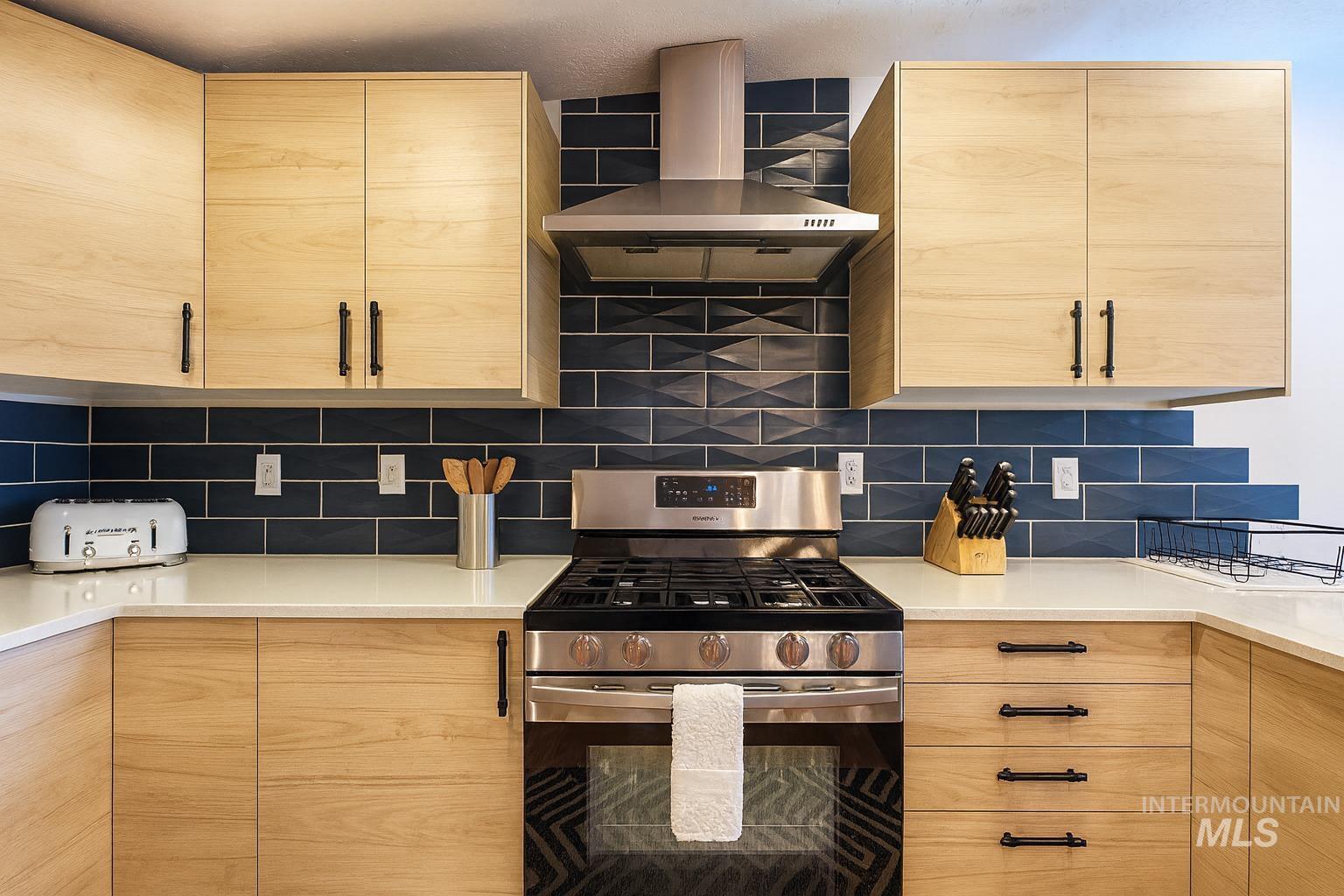 Kitchen featuring light brown cabinetry, stainless steel gas stove, exhaust hood, and tasteful backsplash