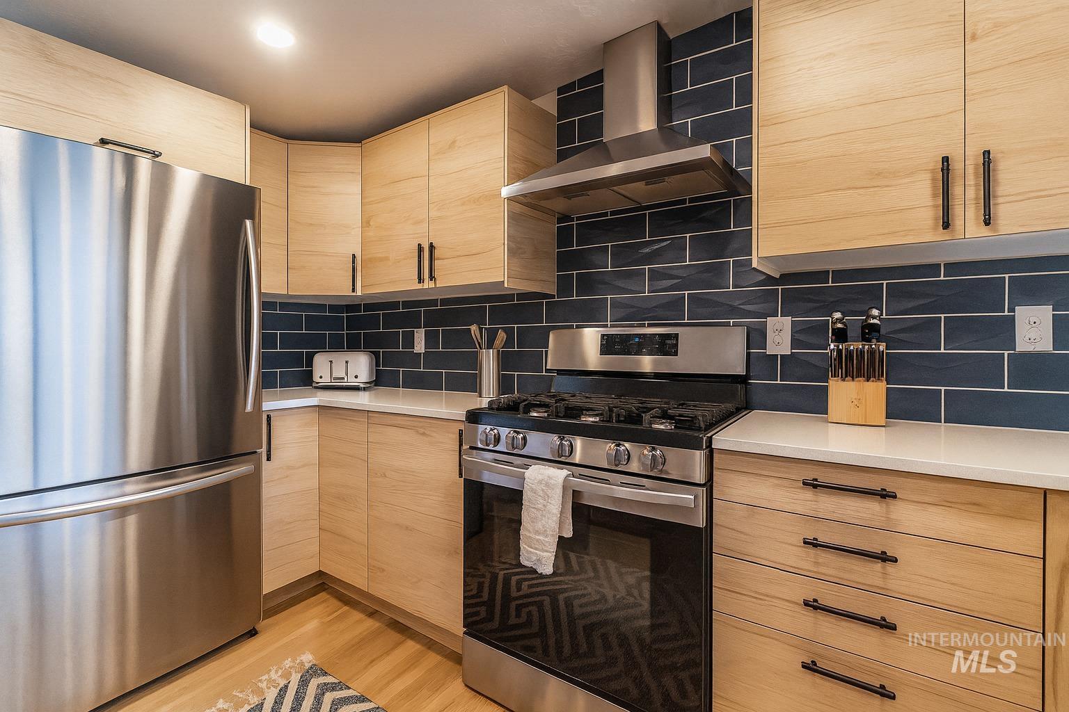 Kitchen featuring stainless steel appliances, light brown cabinets, wall chimney range hood, and modern cabinets