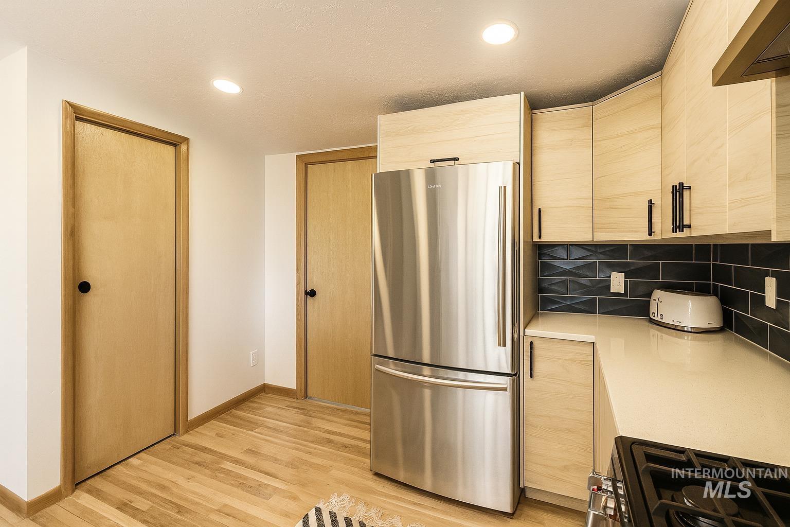 Kitchen with light brown cabinets, freestanding refrigerator, black gas stove, light wood finished floors, and modern cabinets