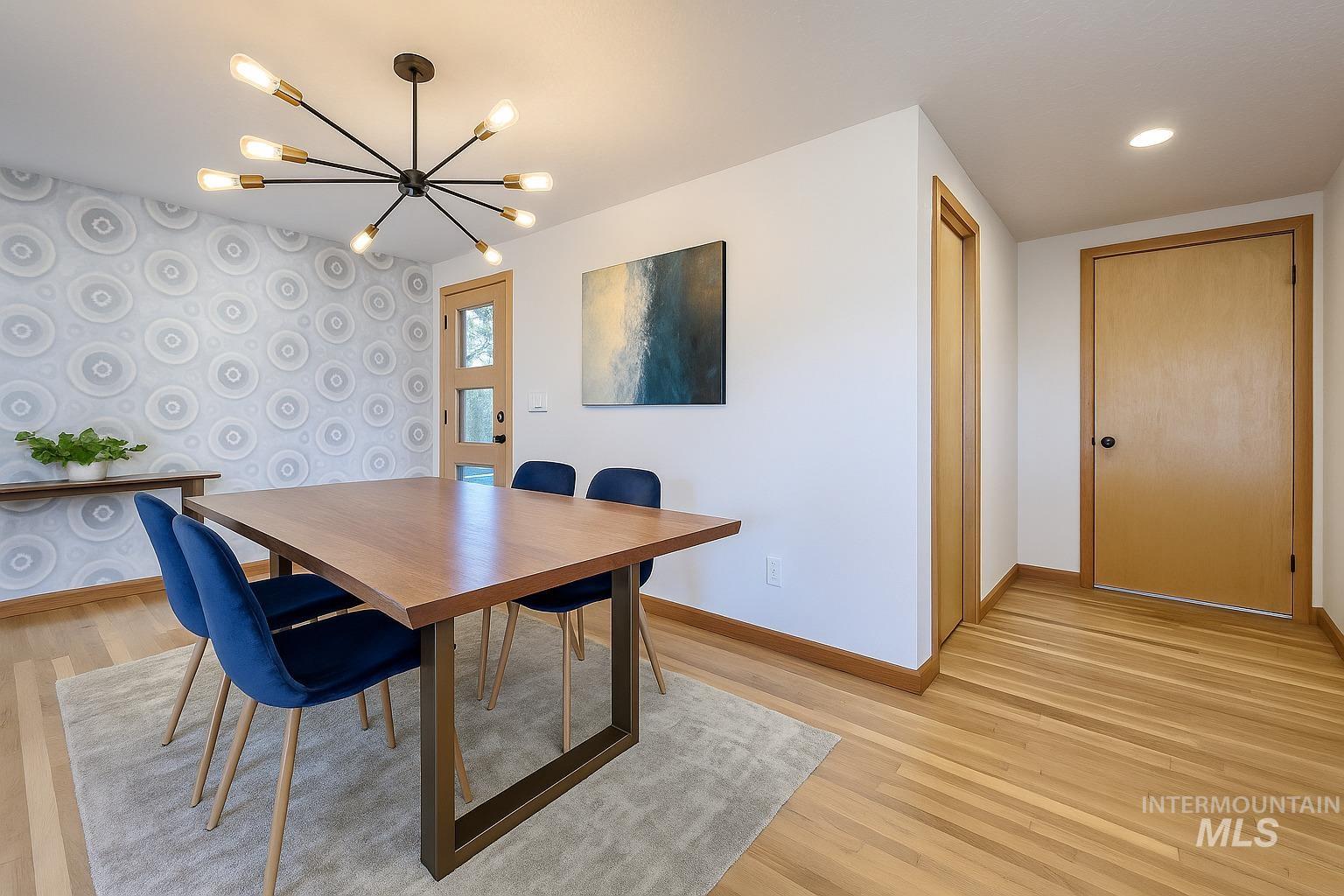 Dining area featuring light wood-type flooring, an accent wall, wallpapered walls, and a chandelier