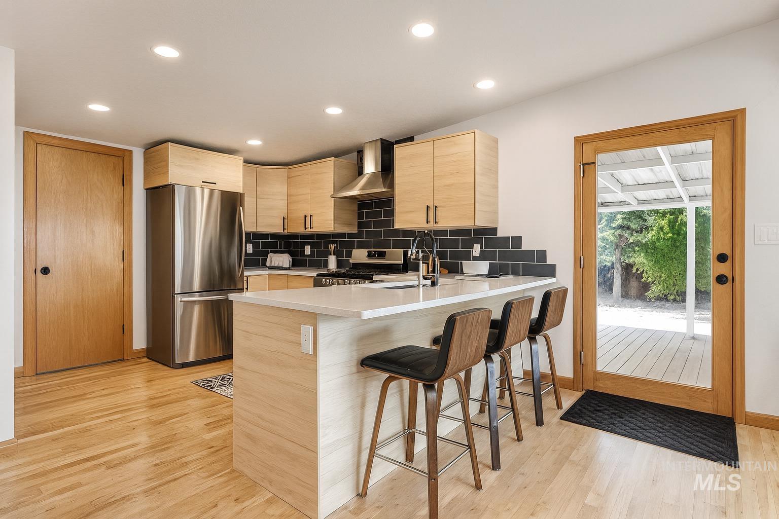 Kitchen featuring stainless steel appliances, light brown cabinetry, backsplash, a breakfast bar, and a peninsula
