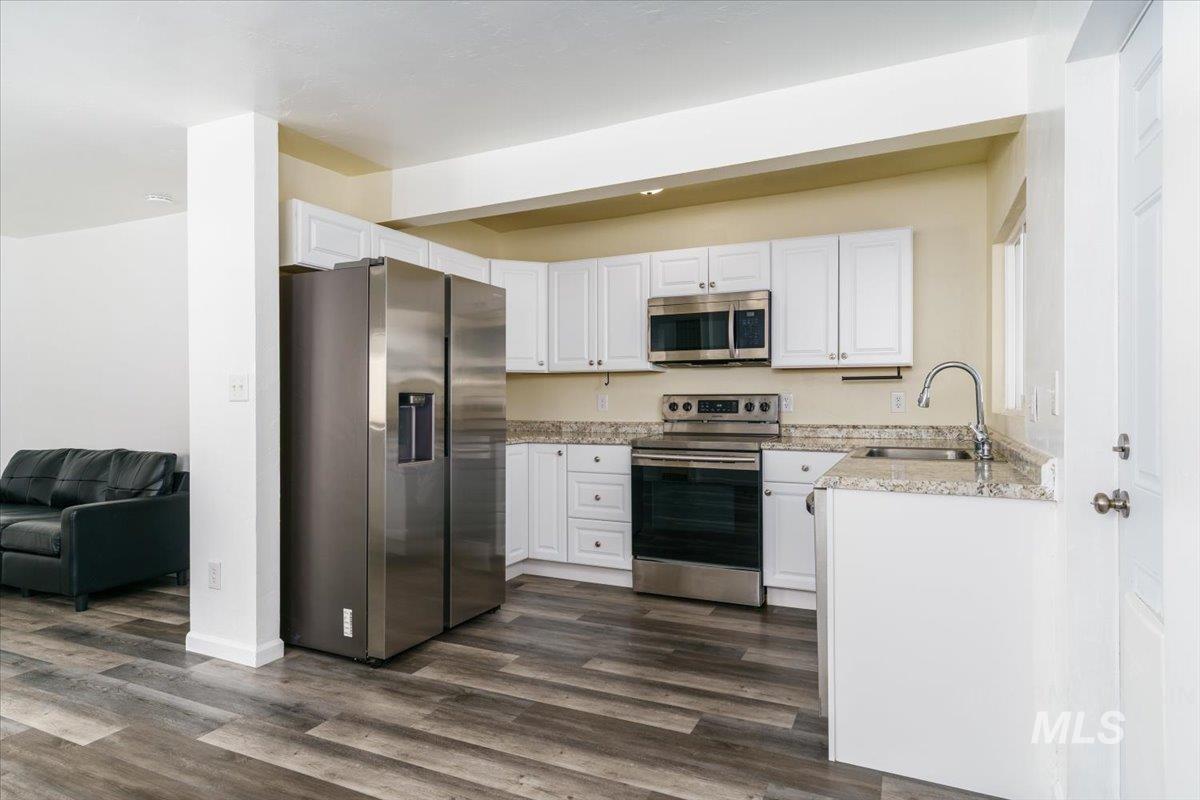 Kitchen with stainless steel appliances, white cabinetry, and dark wood finished floors