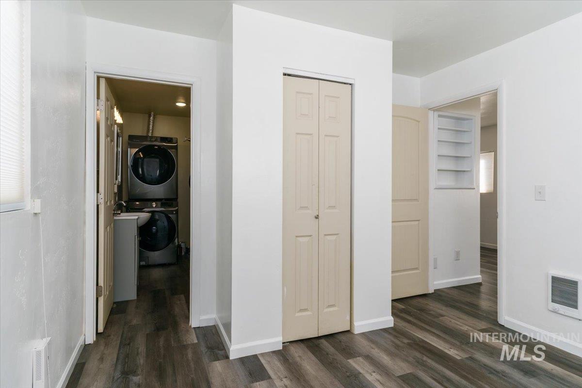 Laundry room with stacked washer / drying machine, dark wood-style flooring, and heating unit