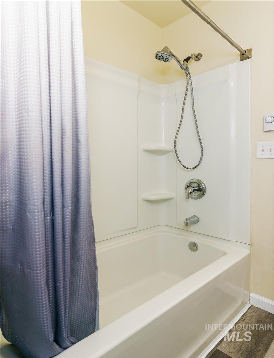 Full bath with shower / bath combination with curtain and wood finished floors