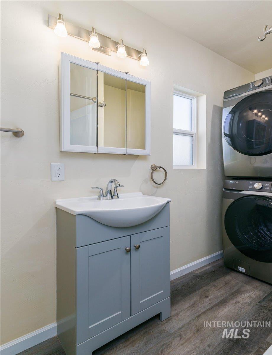 Bathroom with dark wood-style flooring, vanity, and stacked washer / drying machine