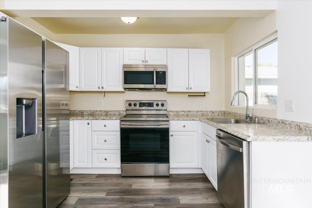 Kitchen with stainless steel appliances, white cabinets, dark wood-type flooring, and light stone countertops