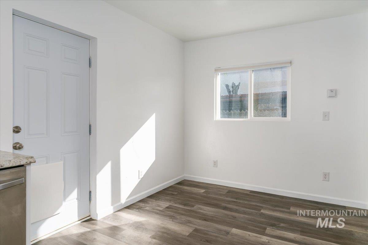 Spare room featuring dark wood-style flooring and baseboards