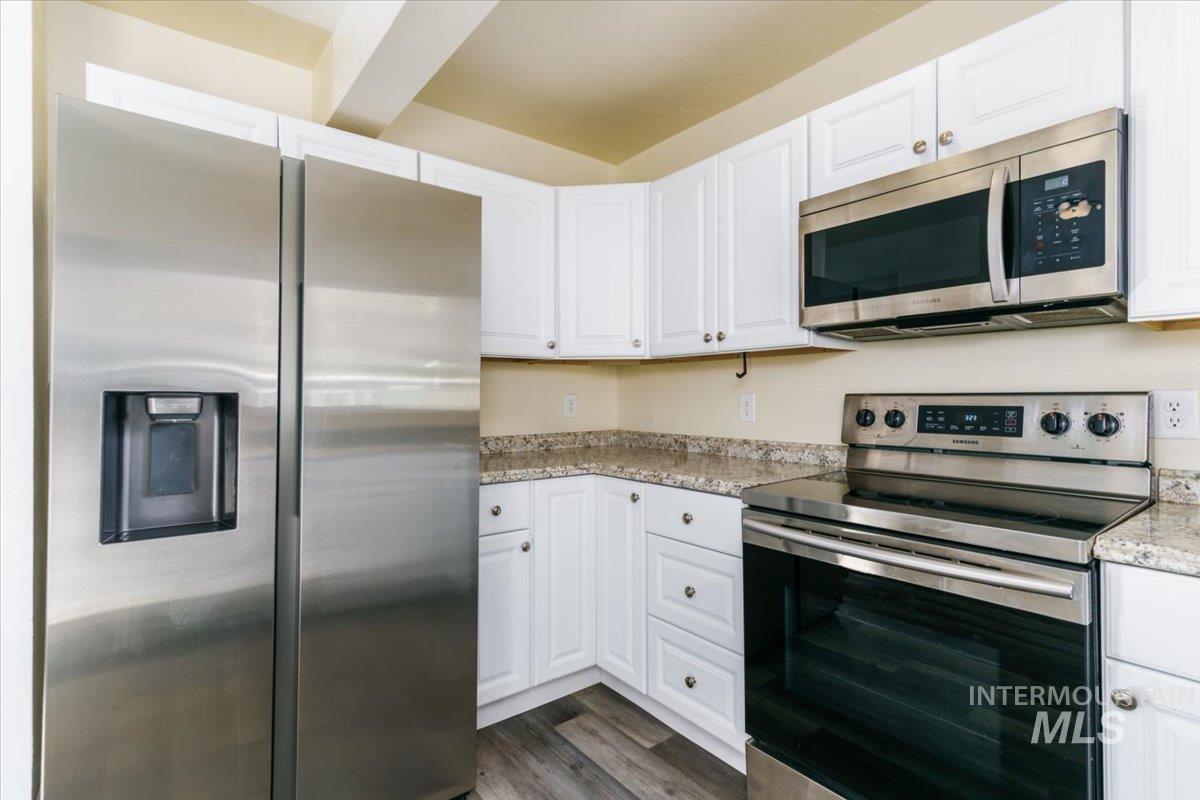 Kitchen with appliances with stainless steel finishes, white cabinetry, dark wood-type flooring, and light stone countertops