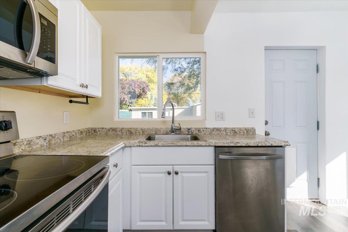 Kitchen featuring stainless steel appliances, white cabinets, light wood-style floors, and light stone countertops