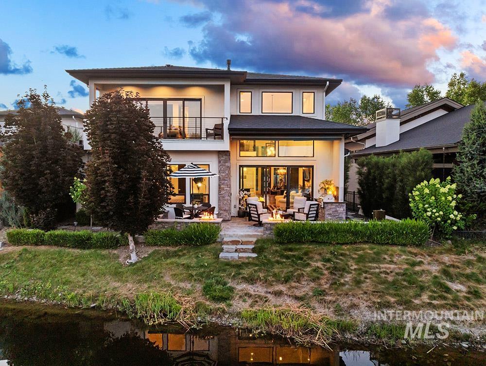 Back of property at dusk featuring an outdoor living space, a balcony, a patio area, stucco siding, and a water view