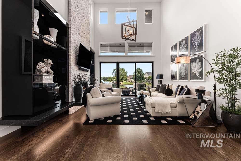 Living area with a chandelier, wood finished floors, a high ceiling, healthy amount of natural light, and a stone fireplace