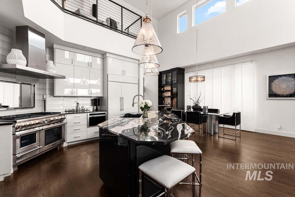 Kitchen featuring range with two ovens, wall chimney exhaust hood, dark wood finished floors, a towering ceiling, and a breakfast bar