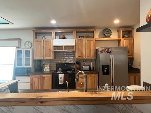 Kitchen with decorative backsplash, black electric range oven, stainless steel refrigerator with ice dispenser, dark countertops, and open shelves