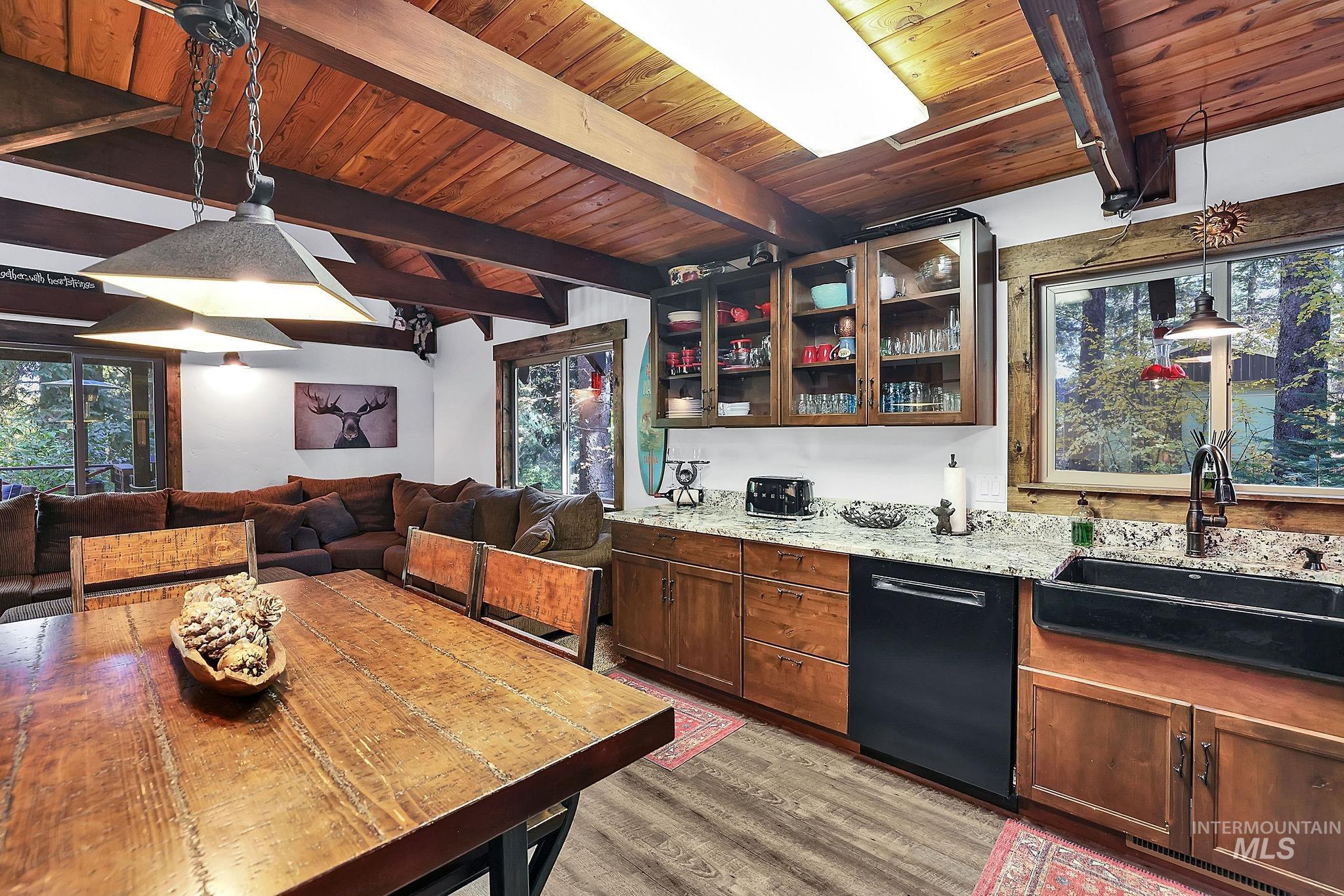 Kitchen with pendant lighting, glass insert cabinets, black dishwasher, open floor plan, and light stone counters