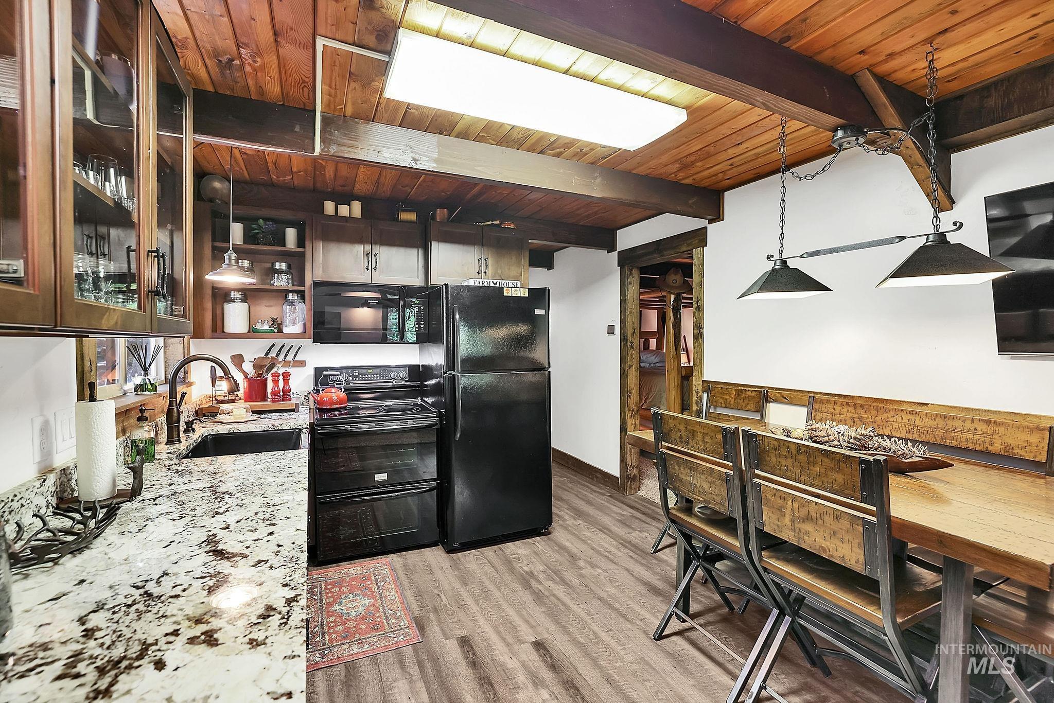 Kitchen with black appliances, light stone countertops, open shelves, light wood-style floors, and glass insert cabinets