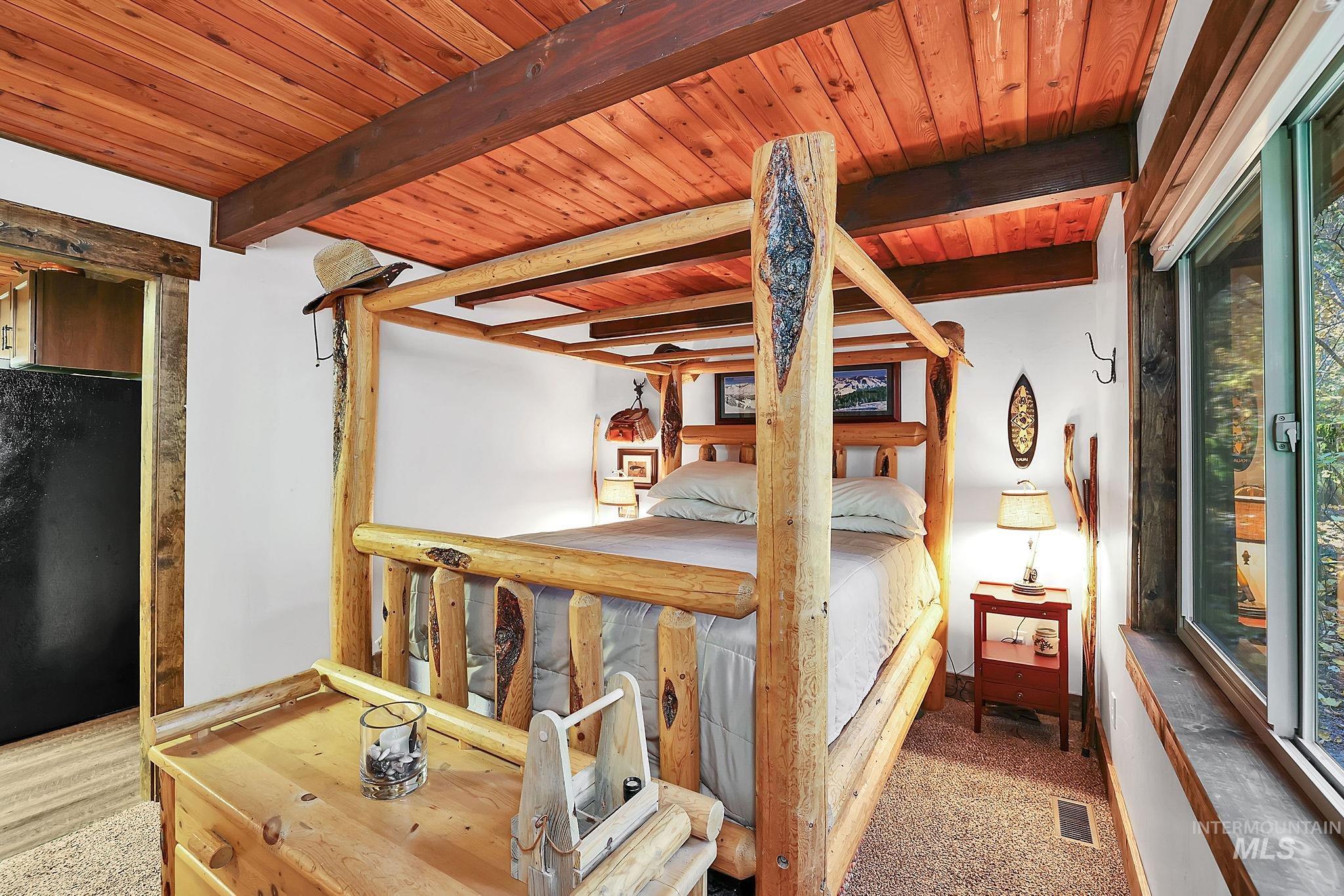 Bedroom featuring freestanding refrigerator, a wooden ceiling with exposed beams, carpet, and multiple windows