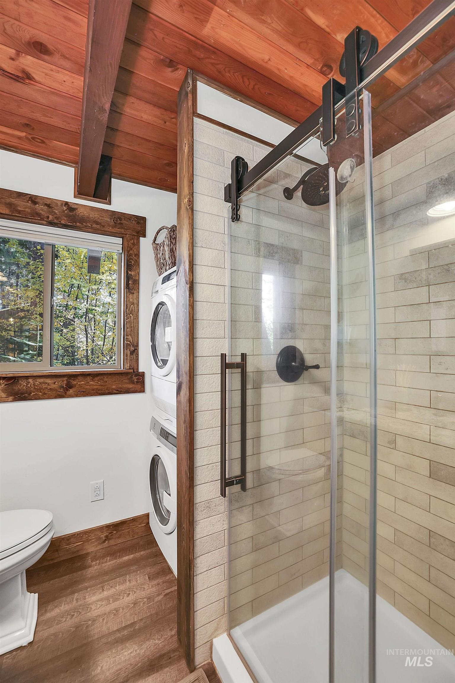 Bathroom with dark wood-style floors, stacked washer / dryer, a shower stall, and a wooden ceiling with exposed beams