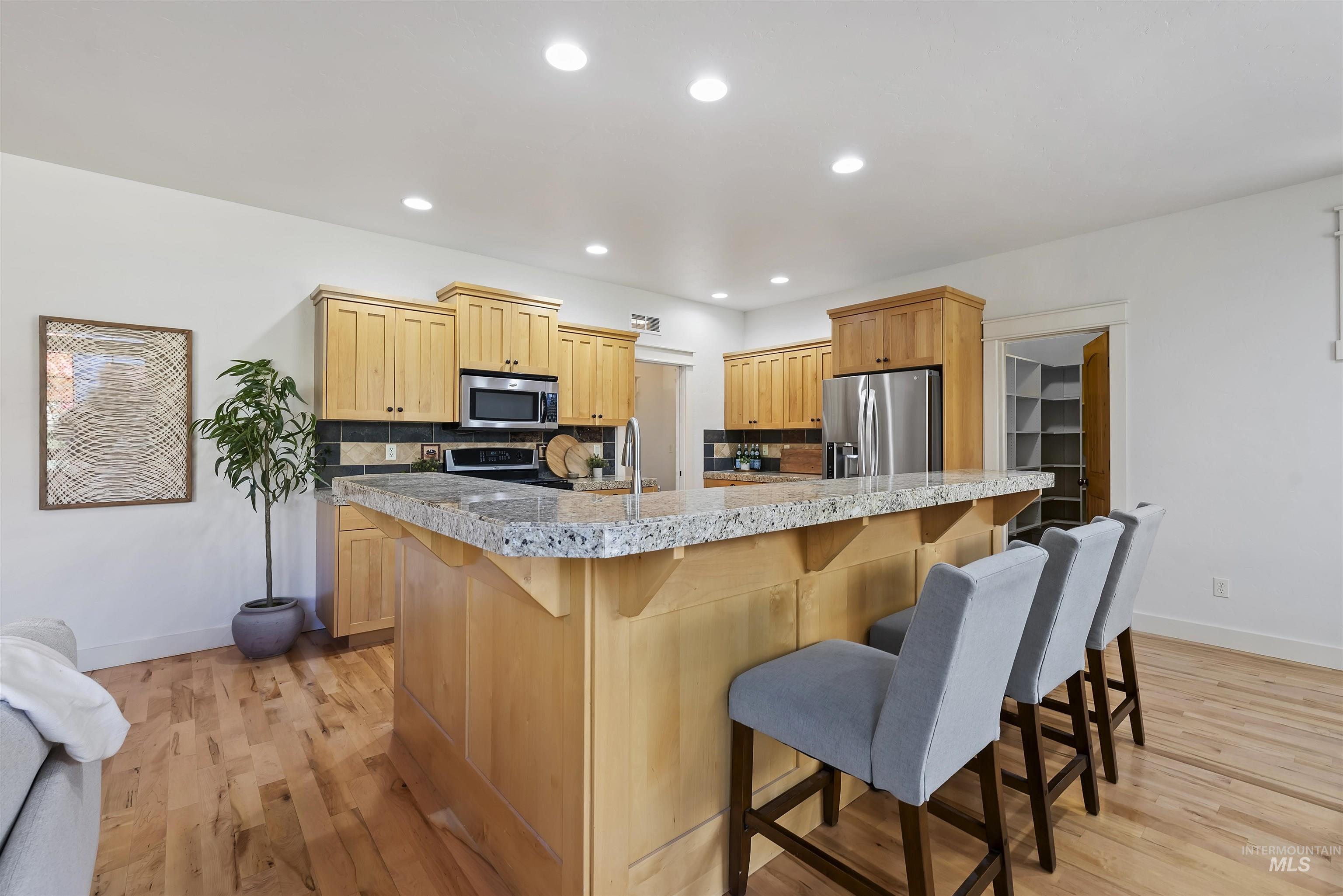Kitchen with a kitchen bar, light wood-style floors, recessed lighting, appliances with stainless steel finishes, and tasteful backsplash