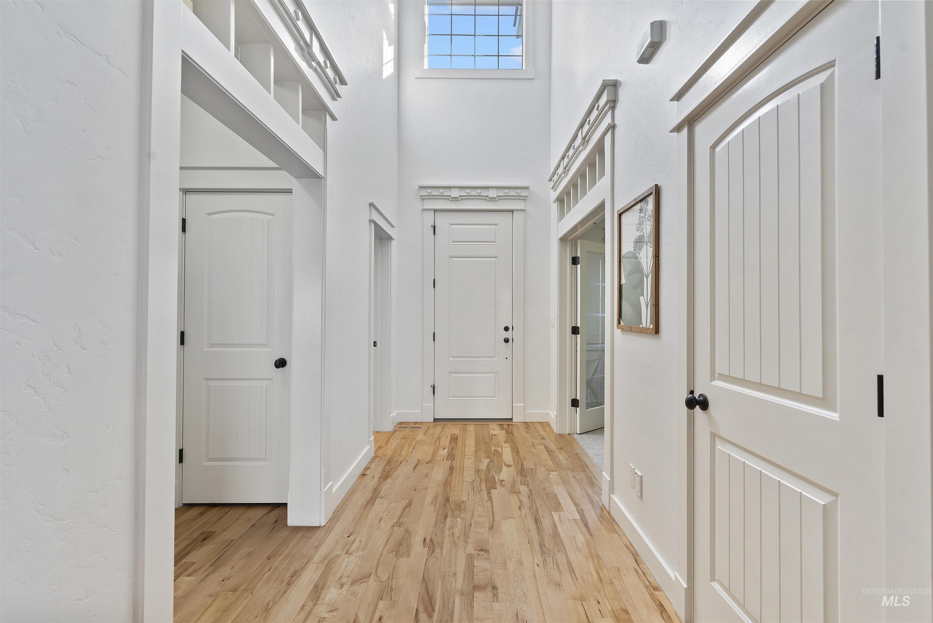 Hallway with light wood-type flooring and a towering ceiling