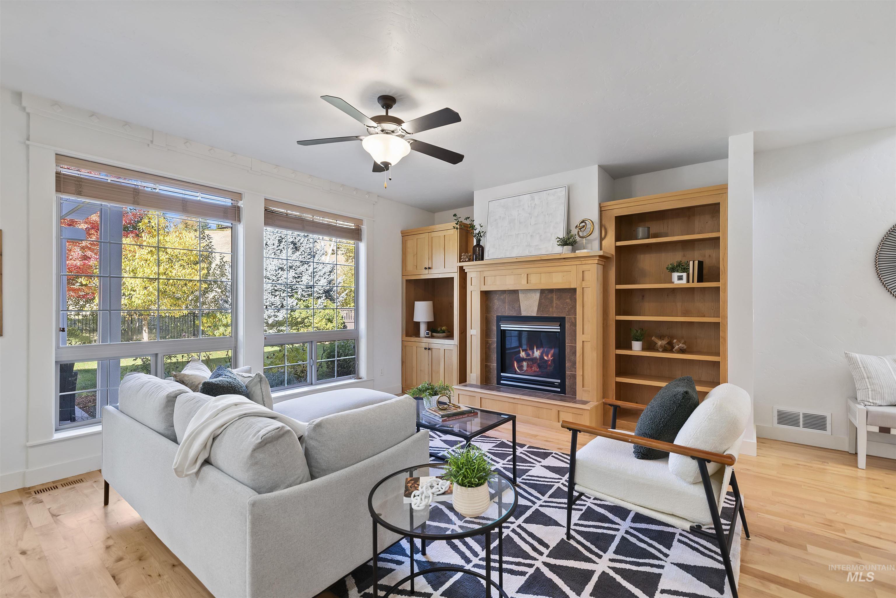 Living area with light wood-style floors, a tiled fireplace, and a ceiling fan