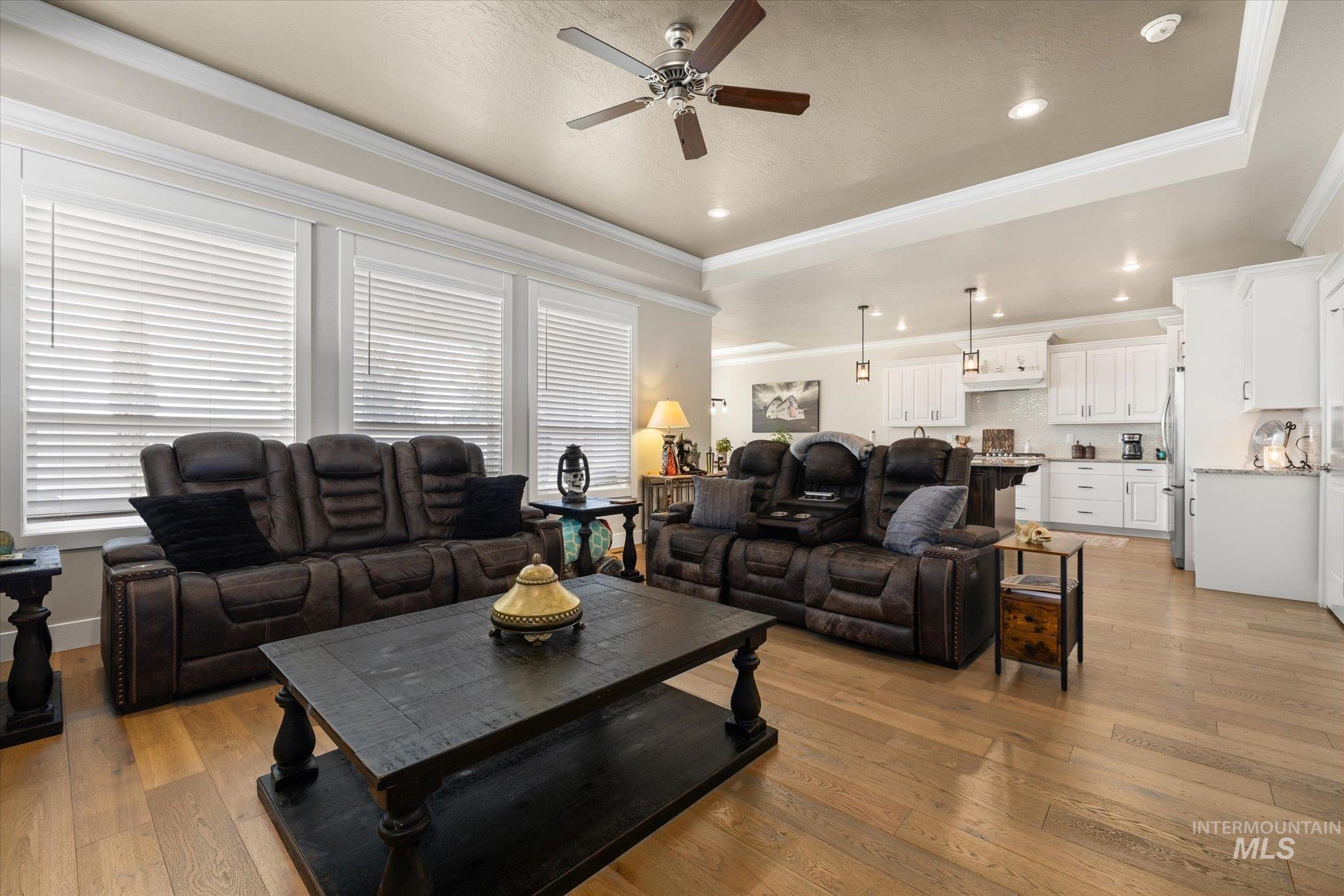Living area with crown molding, light wood finished floors, a raised ceiling, a ceiling fan, and recessed lighting