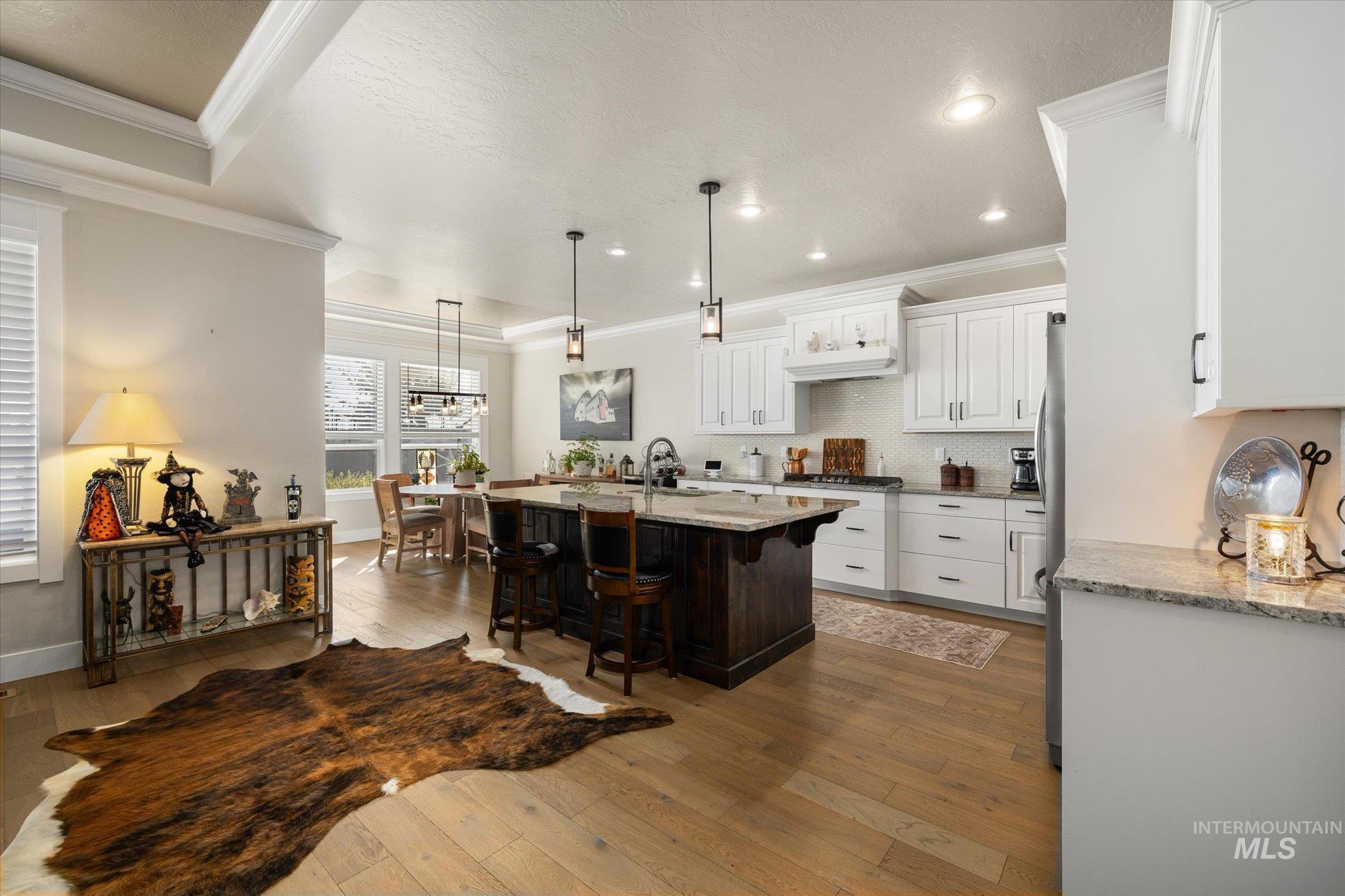 Kitchen featuring white cabinetry, light stone counters, tasteful backsplash, decorative light fixtures, and a breakfast bar area