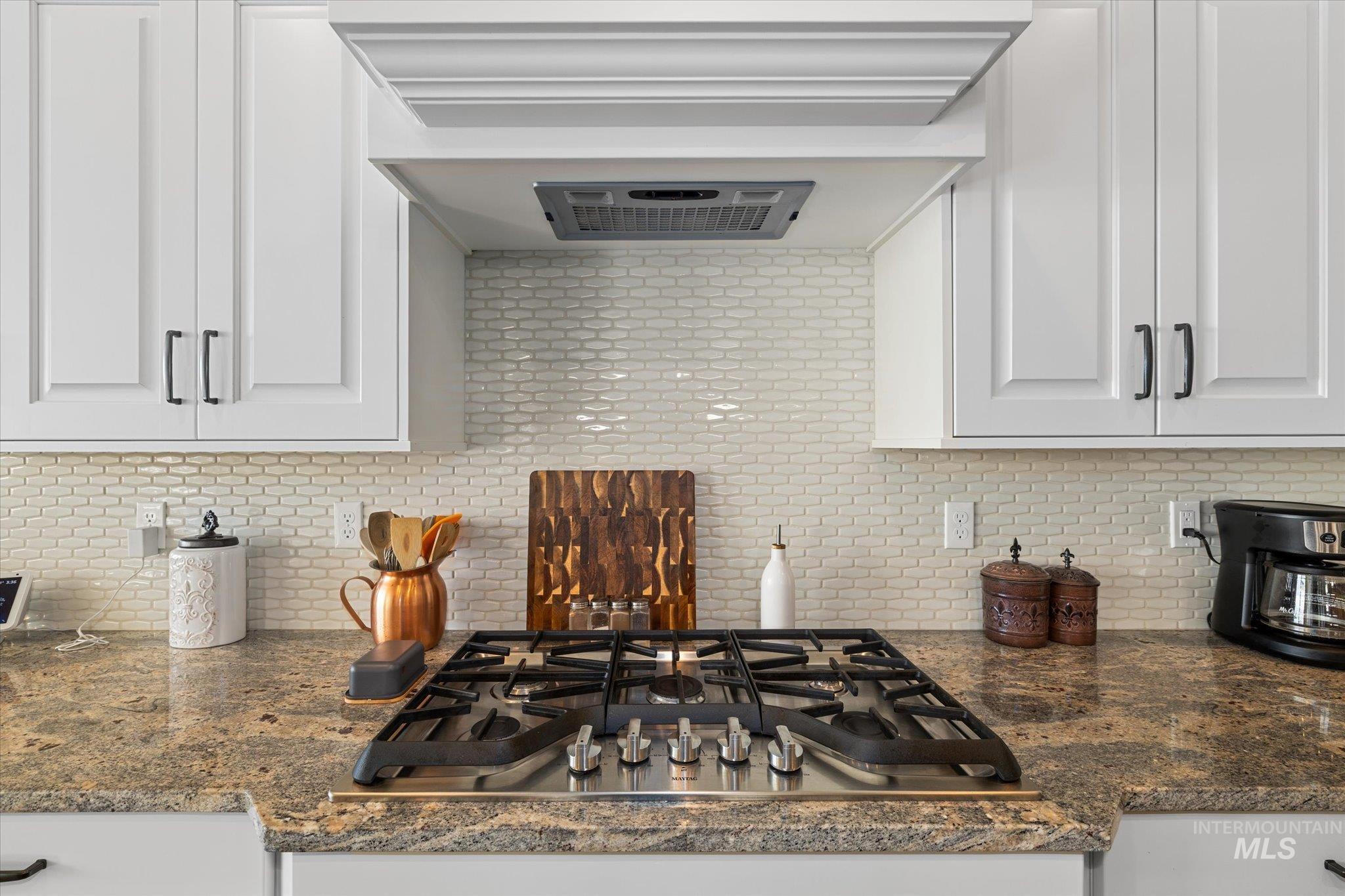 Kitchen featuring exhaust hood, stainless steel gas cooktop, backsplash, and white cabinets