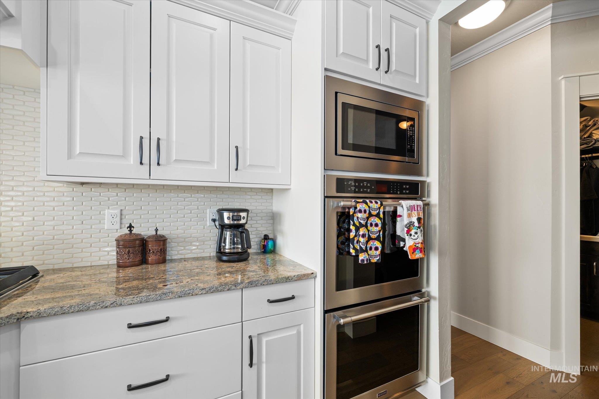 Kitchen with stainless steel appliances, light stone counters, white cabinets, backsplash, and ornamental molding