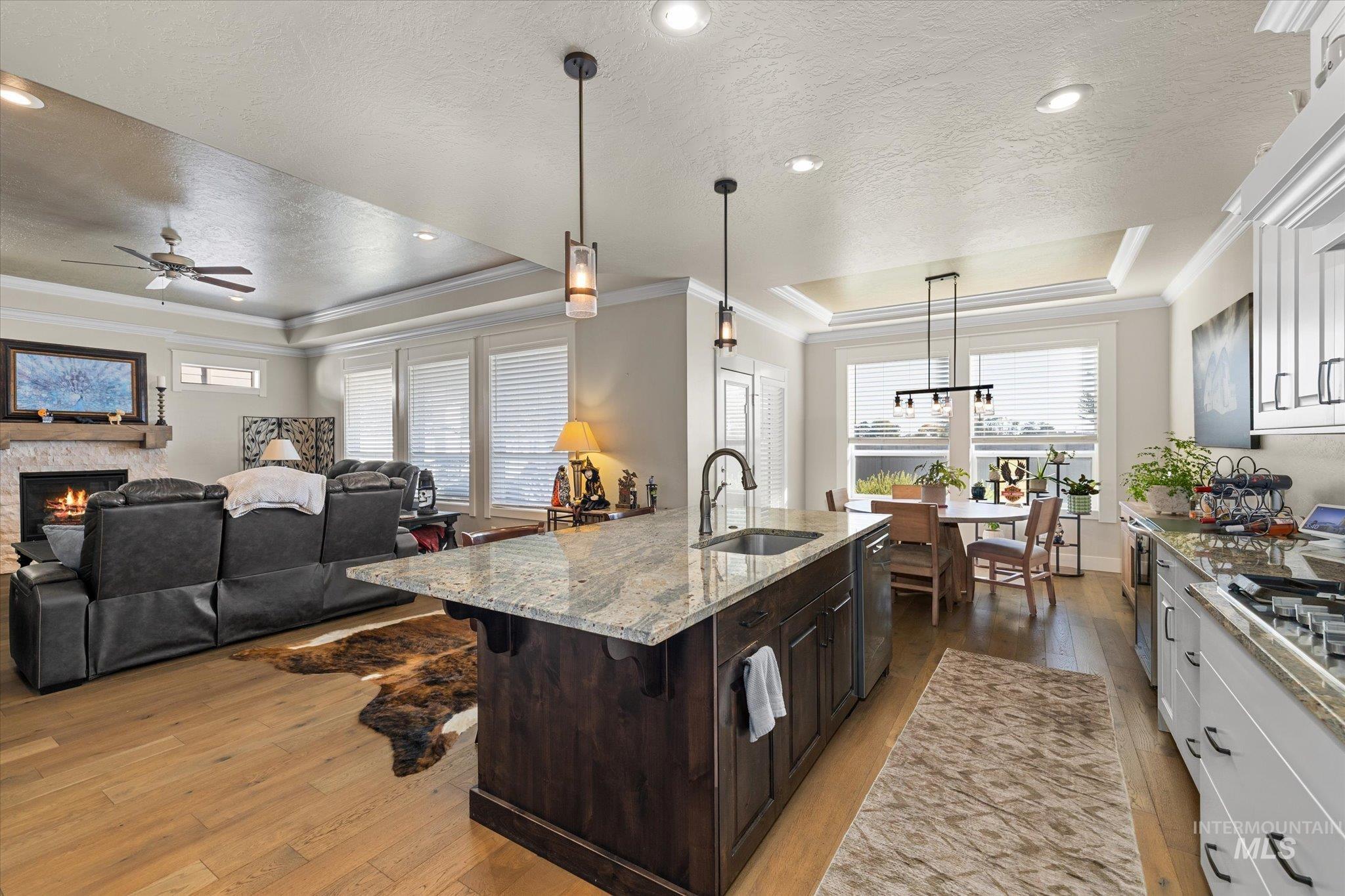 Kitchen with a tray ceiling, crown molding, light wood finished floors, pendant lighting, and dark brown cabinets