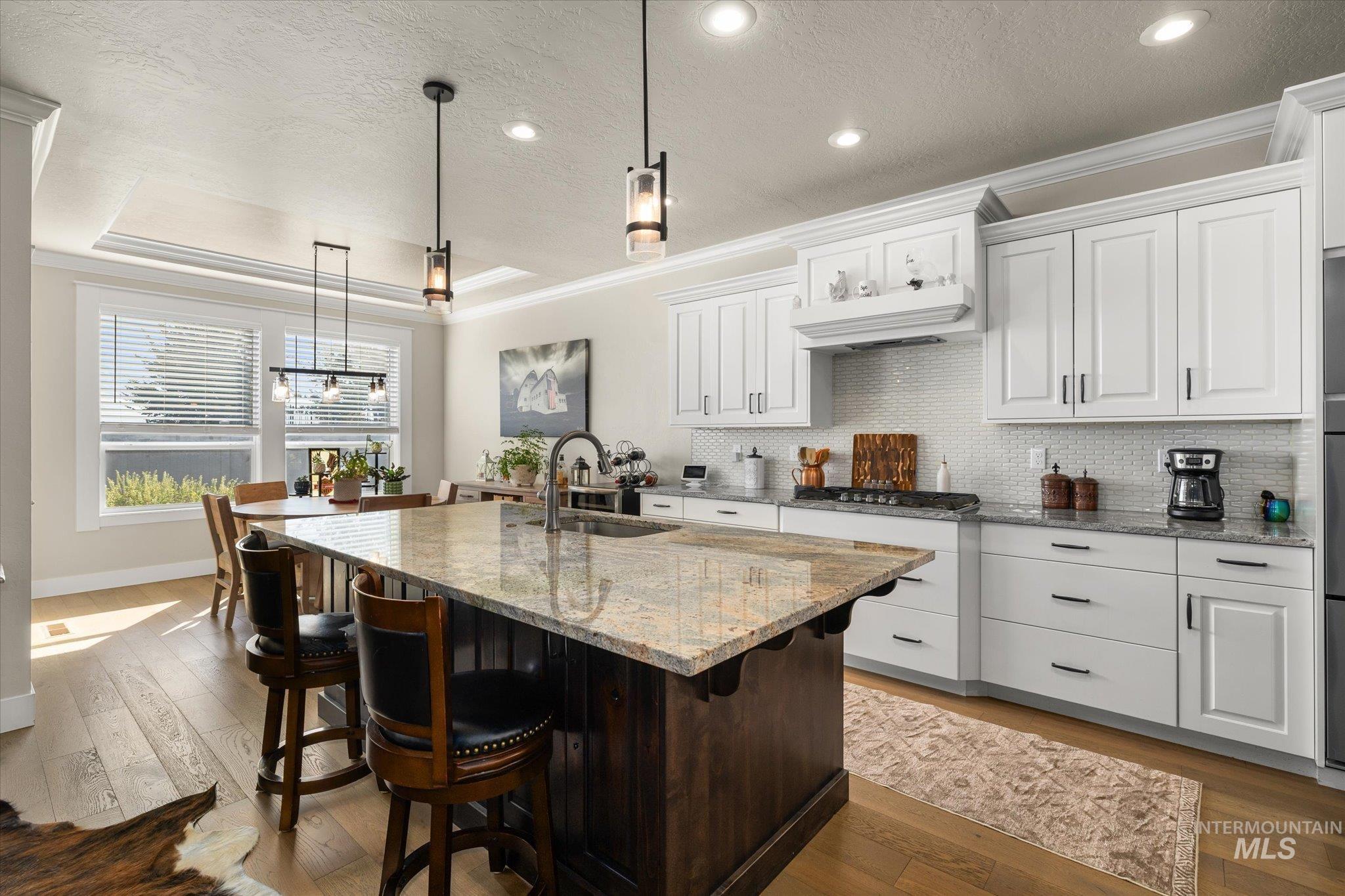 Kitchen with white cabinets, a textured ceiling, light stone counters, ornamental molding, and a kitchen breakfast bar