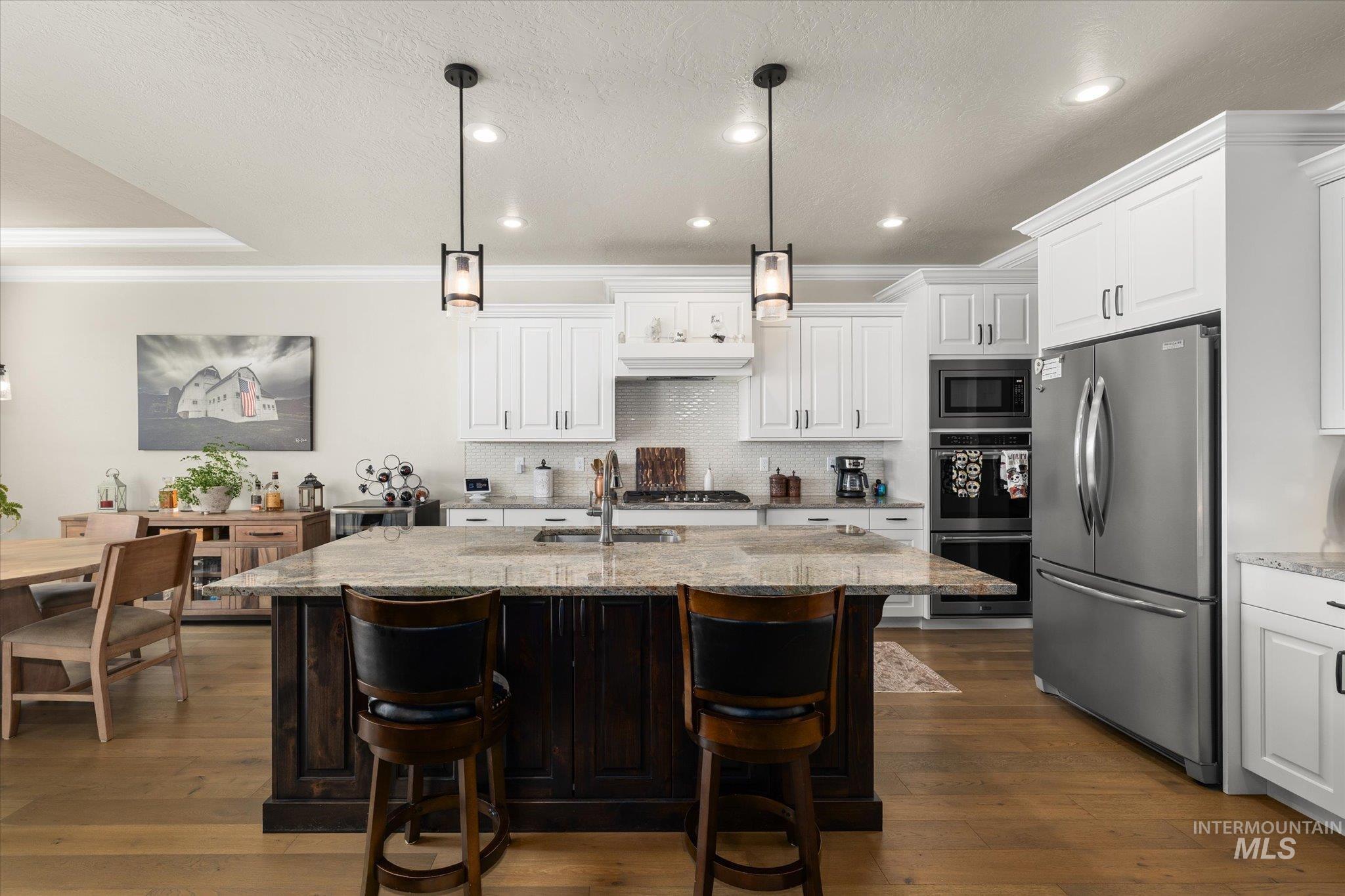 Kitchen featuring stainless steel appliances, light stone countertops, decorative light fixtures, ornamental molding, and dark brown cabinets
