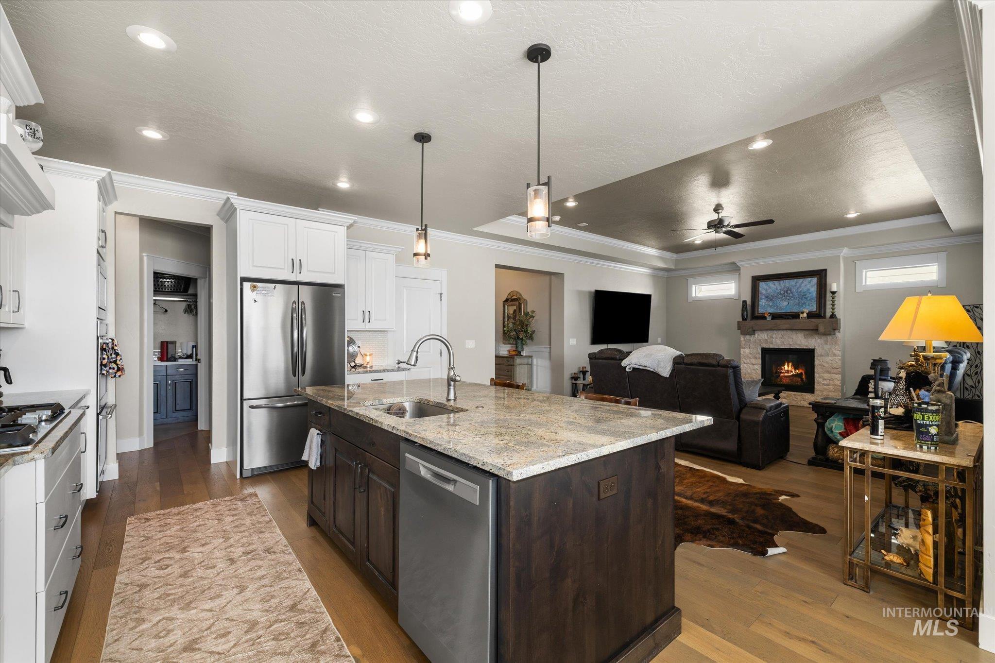 Kitchen featuring hanging light fixtures, a tray ceiling, dark wood finished floors, stainless steel appliances, and ornamental molding