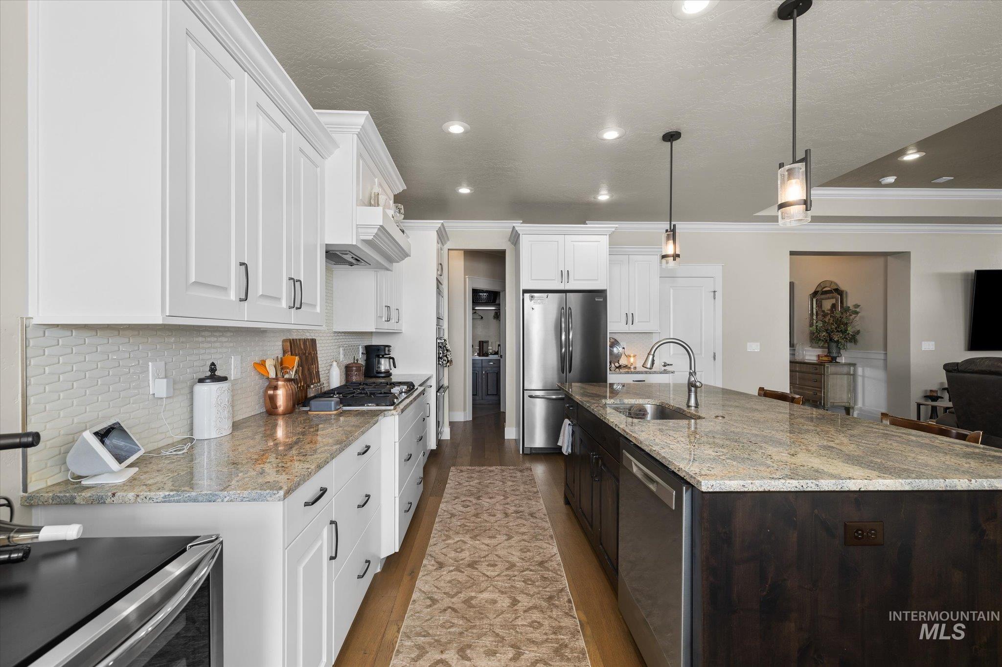 Kitchen with tasteful backsplash, white cabinetry, appliances with stainless steel finishes, dark wood-style flooring, and light stone countertops