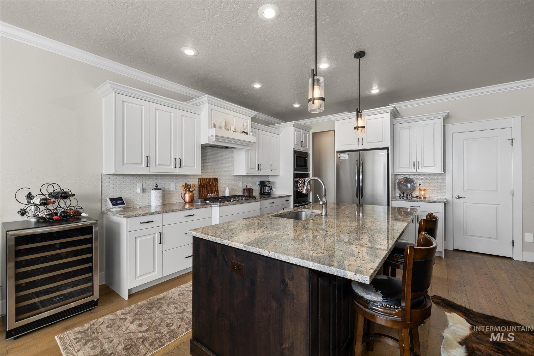 Kitchen featuring crown molding, dark wood finished floors, a center island with sink, beverage cooler, and stainless steel appliances